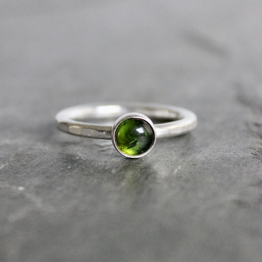 Silver ring with a green tourmaline gemstone on a gray stone surface