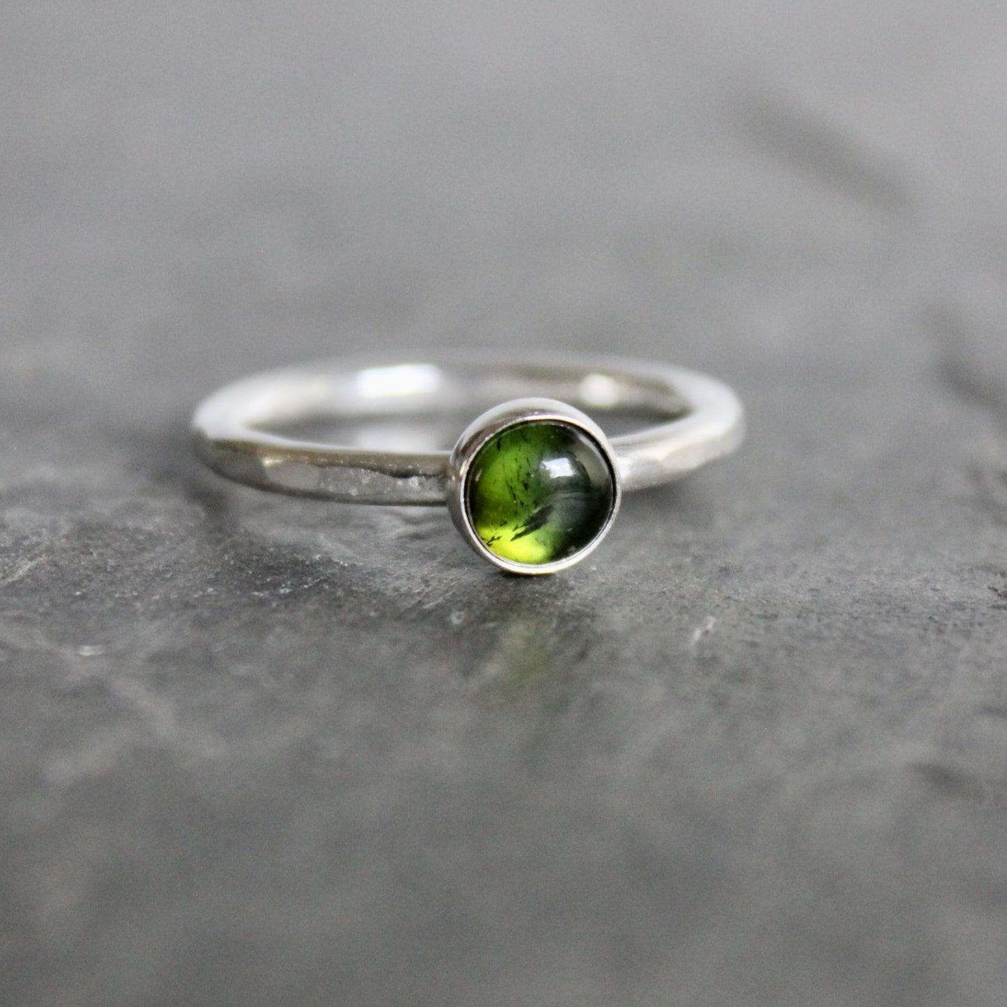 Silver ring with a green tourmaline gemstone on a gray stone surface