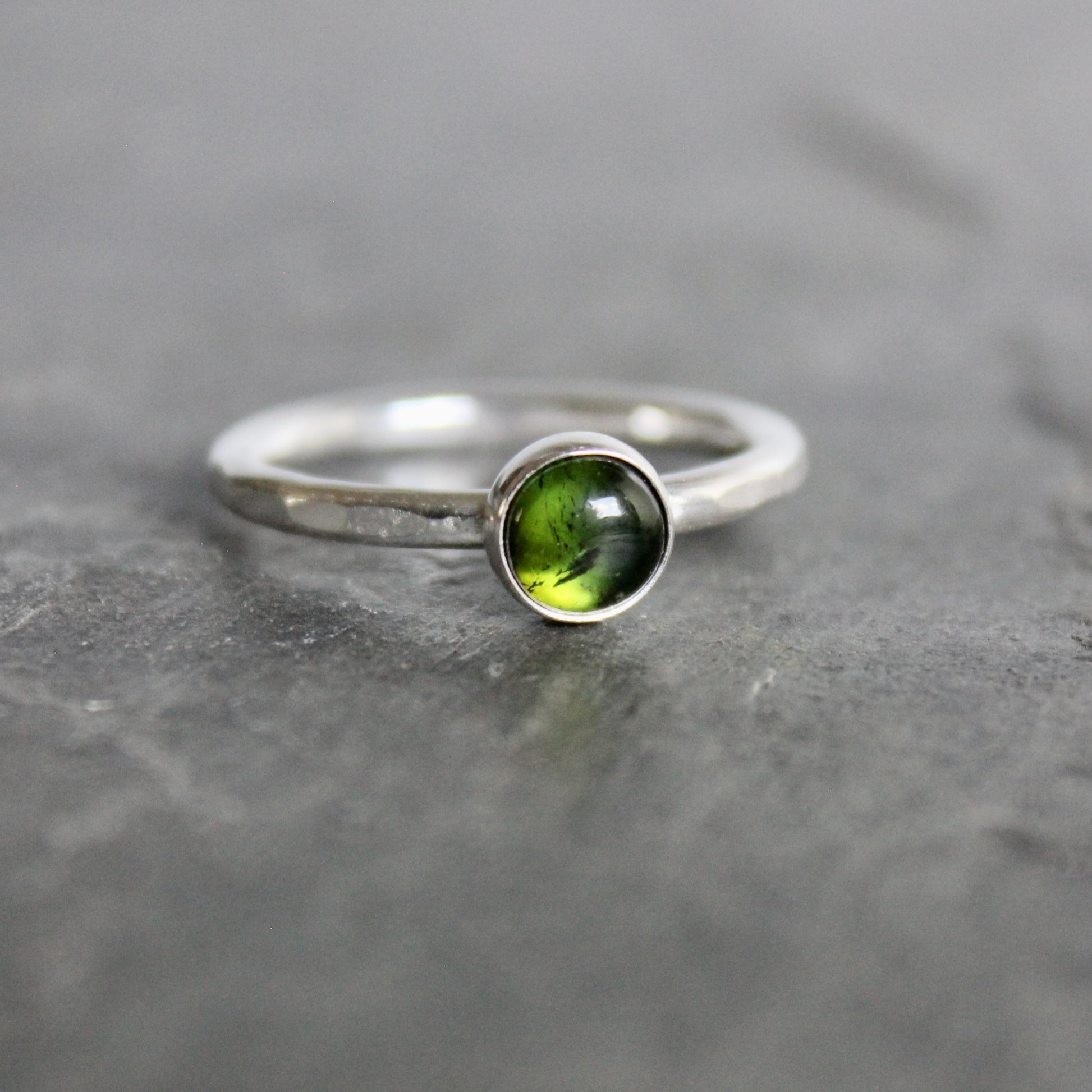Silver ring with a green tourmaline gemstone on a gray stone surface