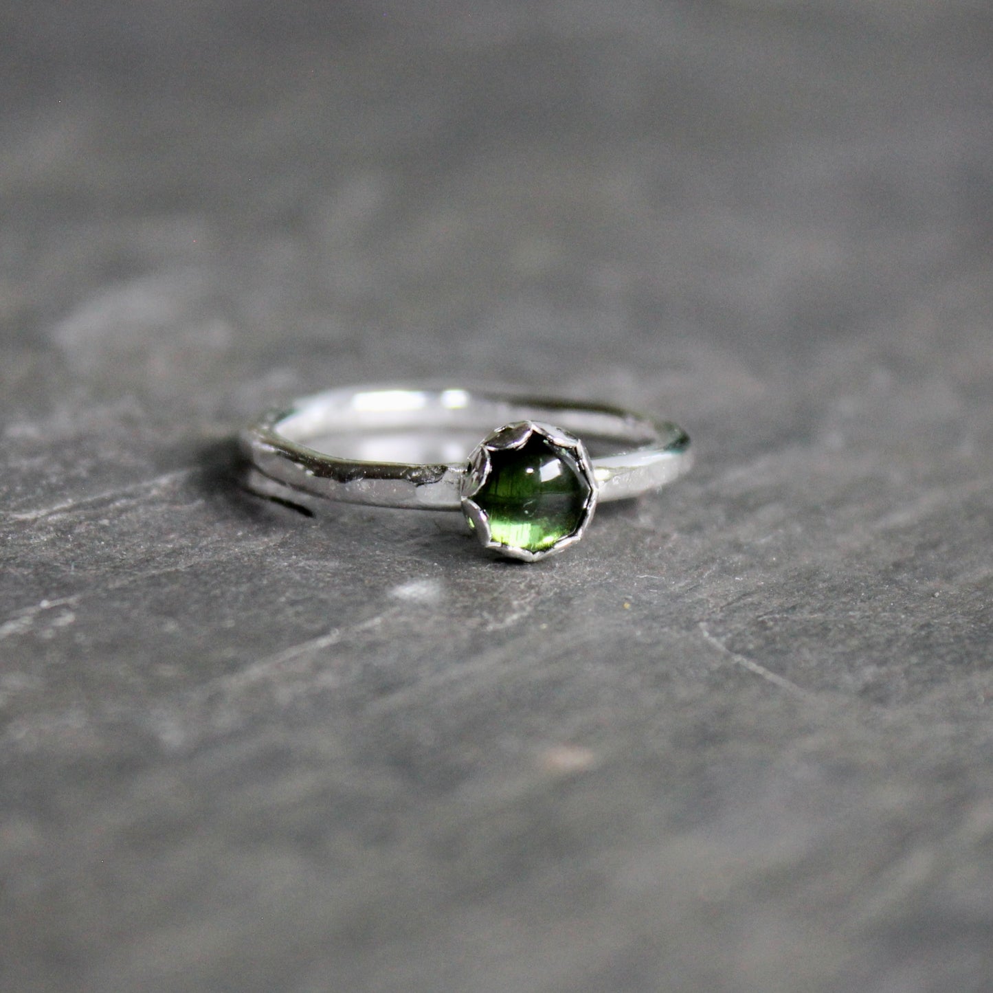Silver ring with a green tourmaline gemstone on a gray stone surface