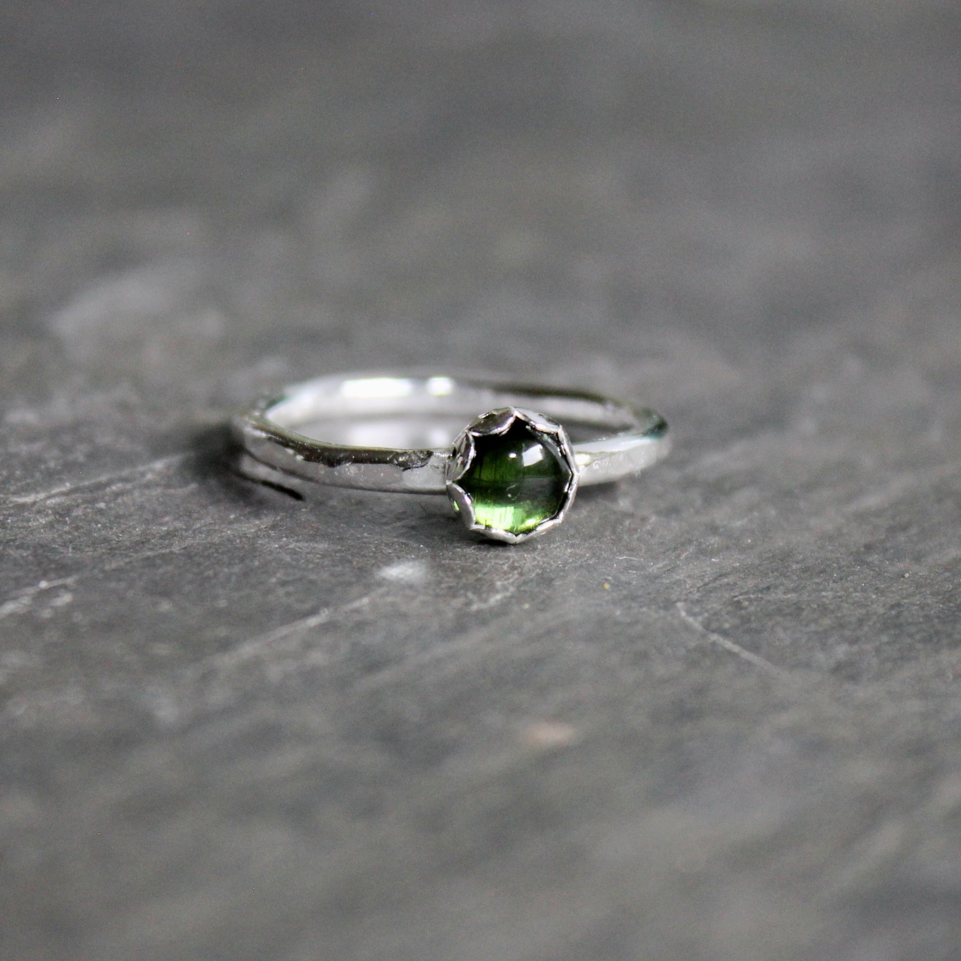 Silver ring with a green tourmaline gemstone on a gray stone surface