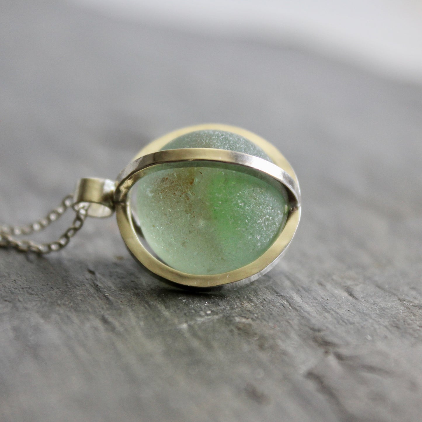 Necklace with a green Japanese Codd Bottle Sea glass pendant on a wooden surface