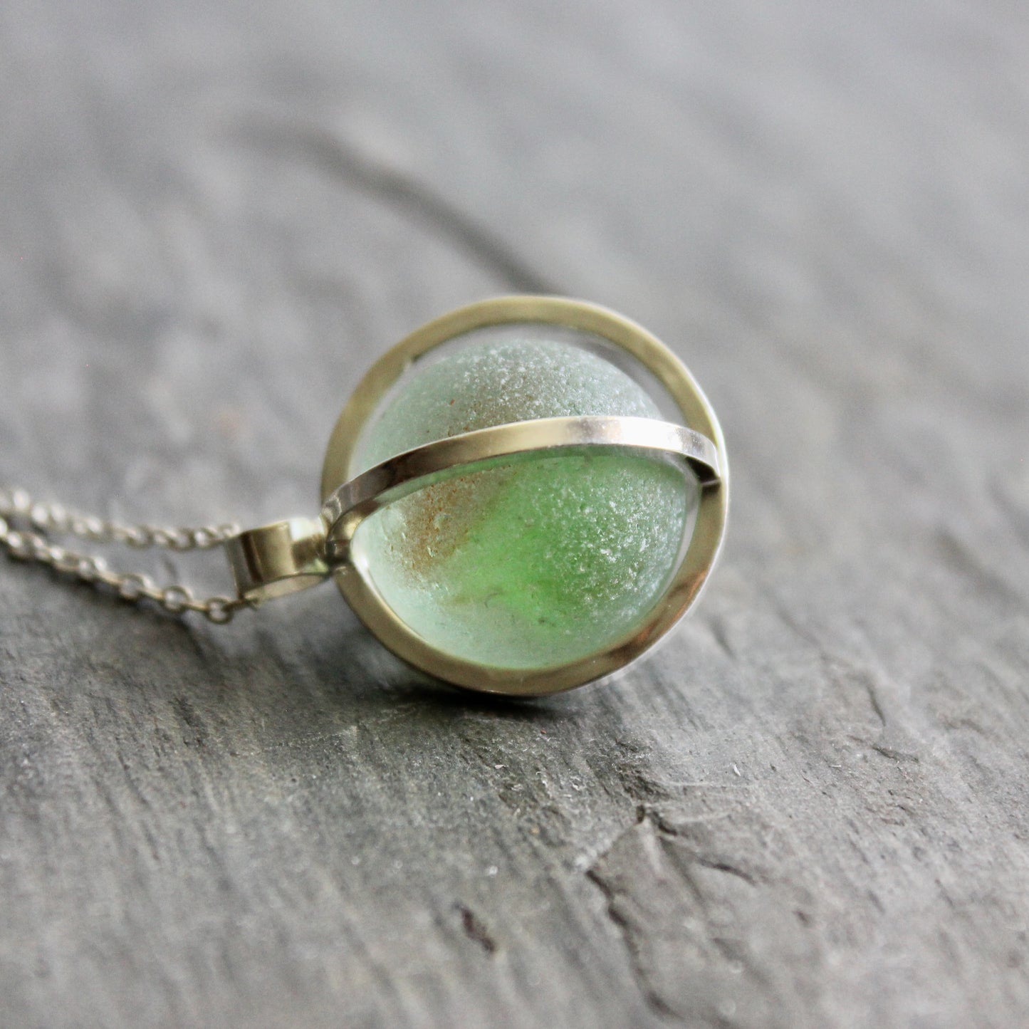 Necklace with a green Japanese Codd Bottle Sea glass pendant on a wooden surface