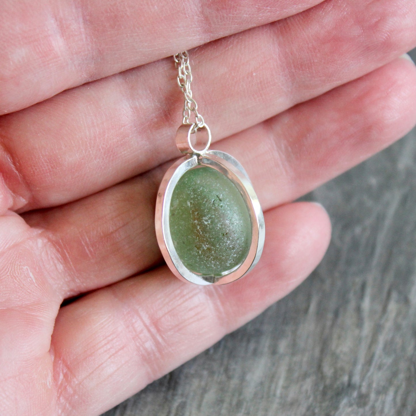 Green Codd Bottle Marble Sea glass pendant on a chain held in a hand against a wooden surface