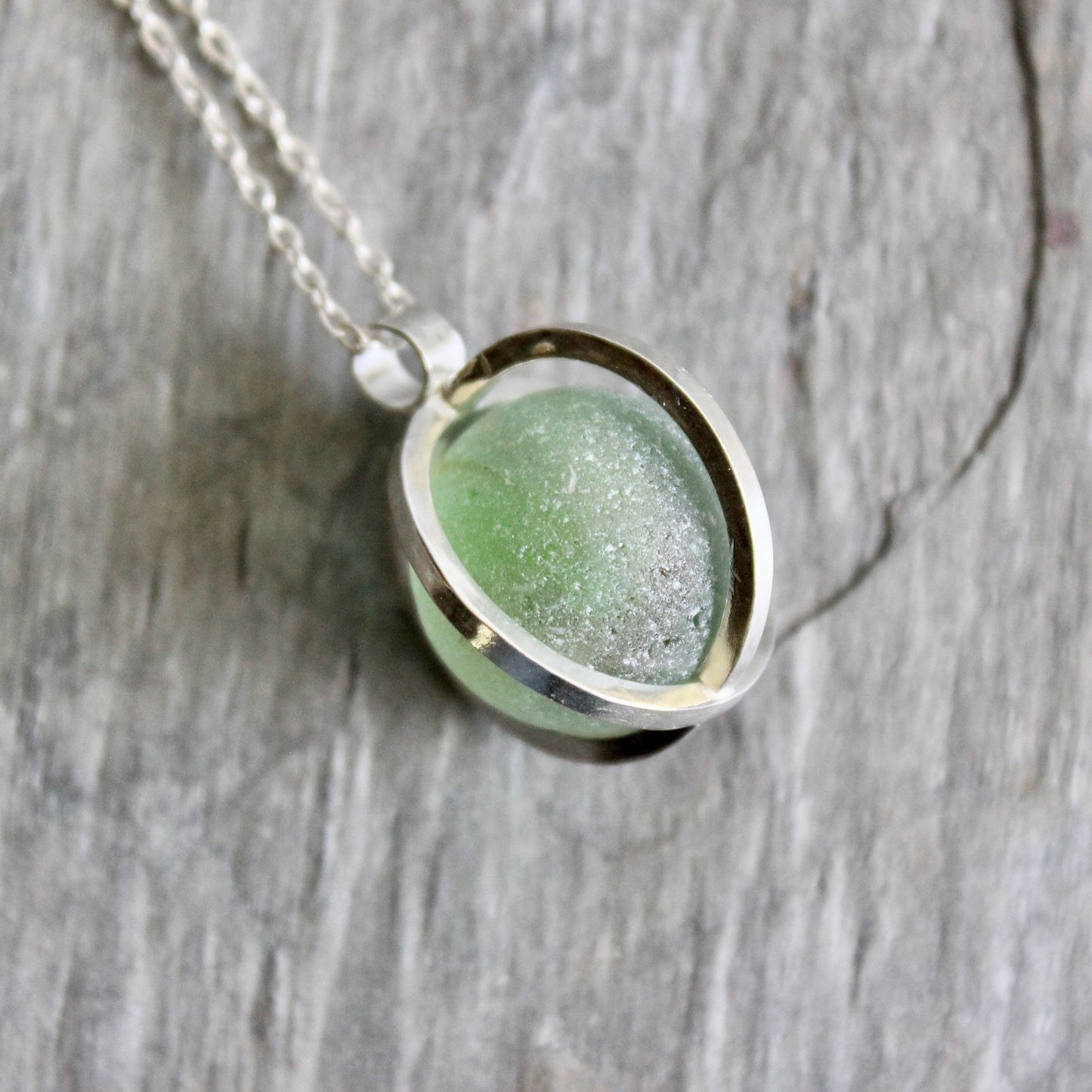Necklace with a green Japanese Codd Bottle Sea glass pendant on a wooden surface