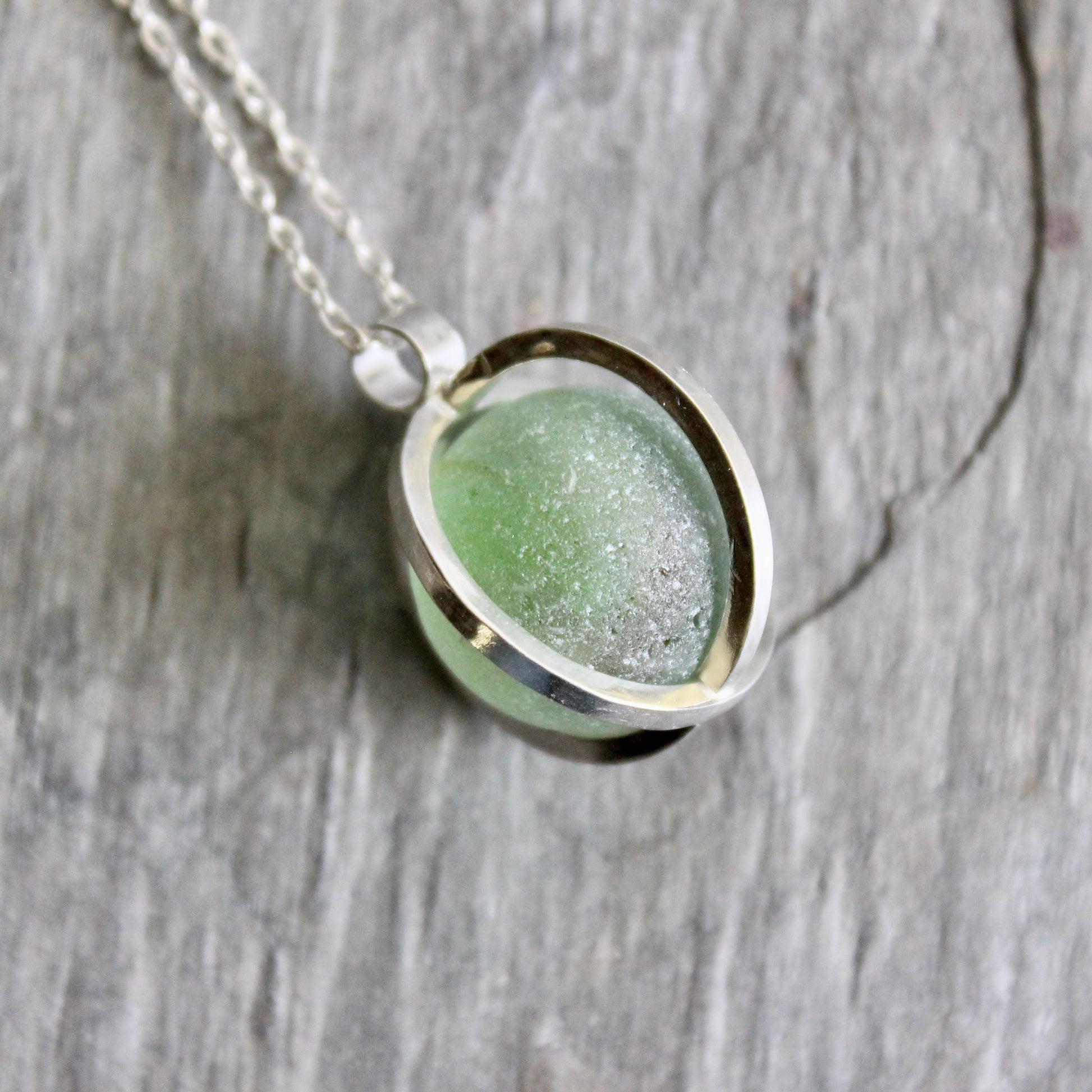 Necklace with a green Japanese Codd Bottle Sea glass pendant on a wooden surface