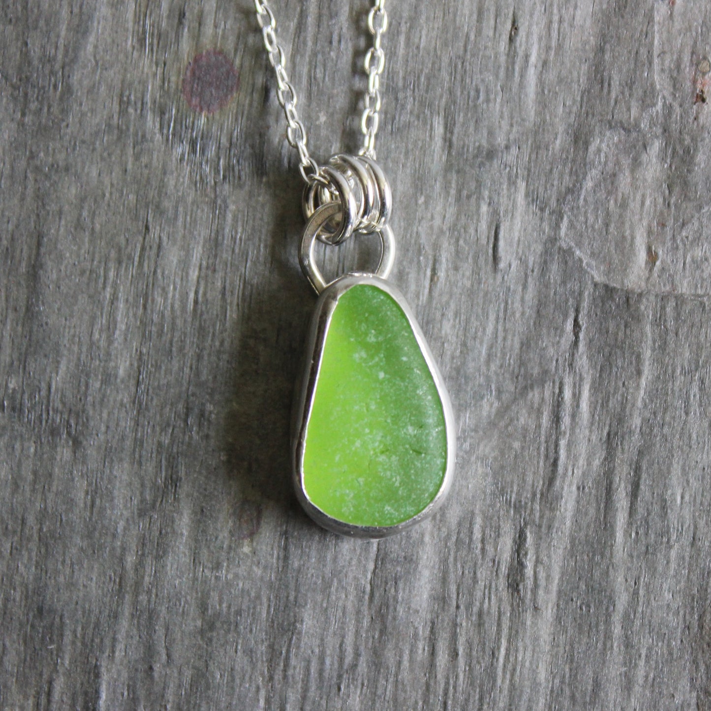 Green teardrop sea glass pendant on a silver chain against a wooden background