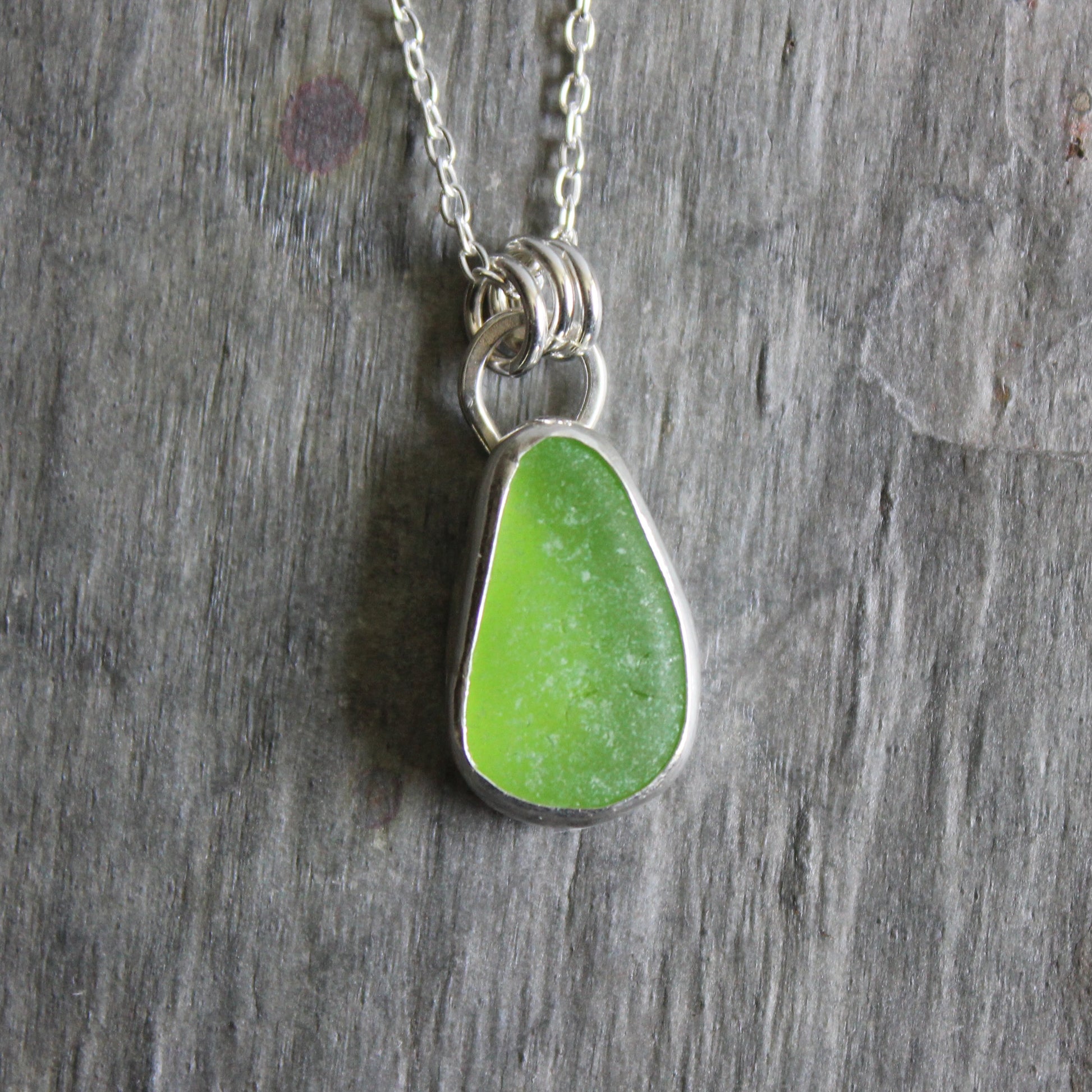 Green teardrop sea glass pendant on a silver chain against a wooden background