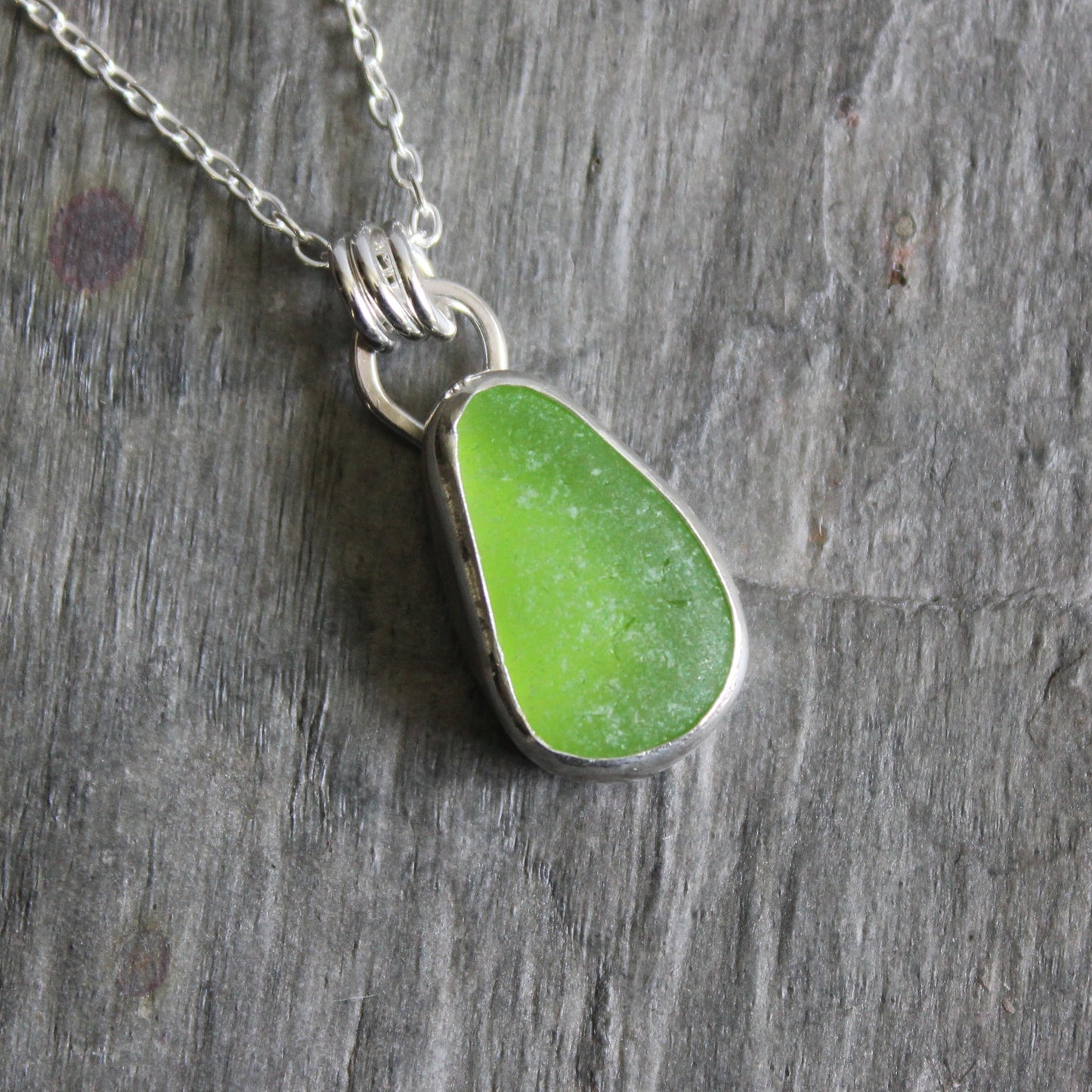 Green sea glass pendant on a silver chain against a wooden background