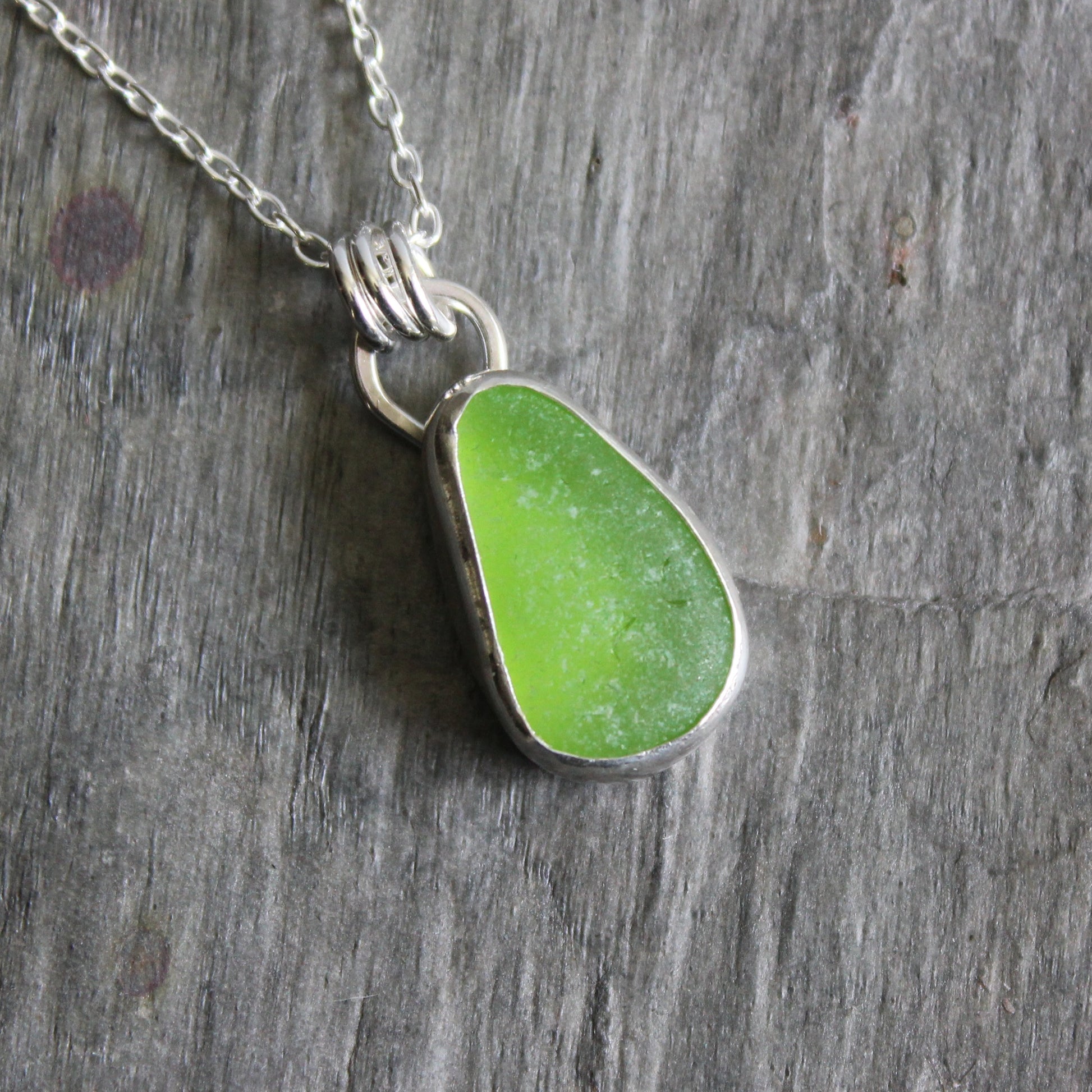 Green sea glass pendant on a silver chain against a wooden background