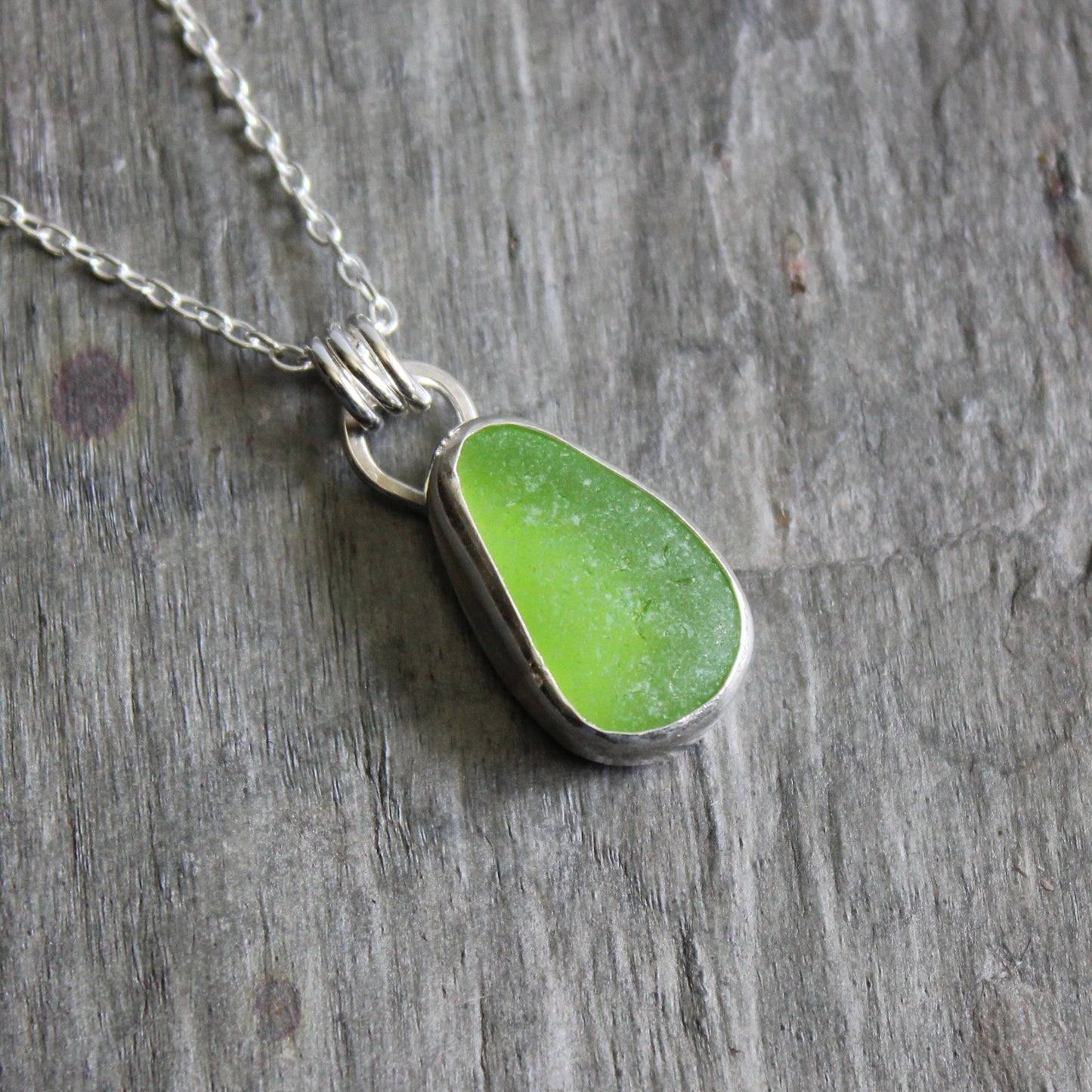 Green sea glass teardrop pendant on a silver chain against a wooden background