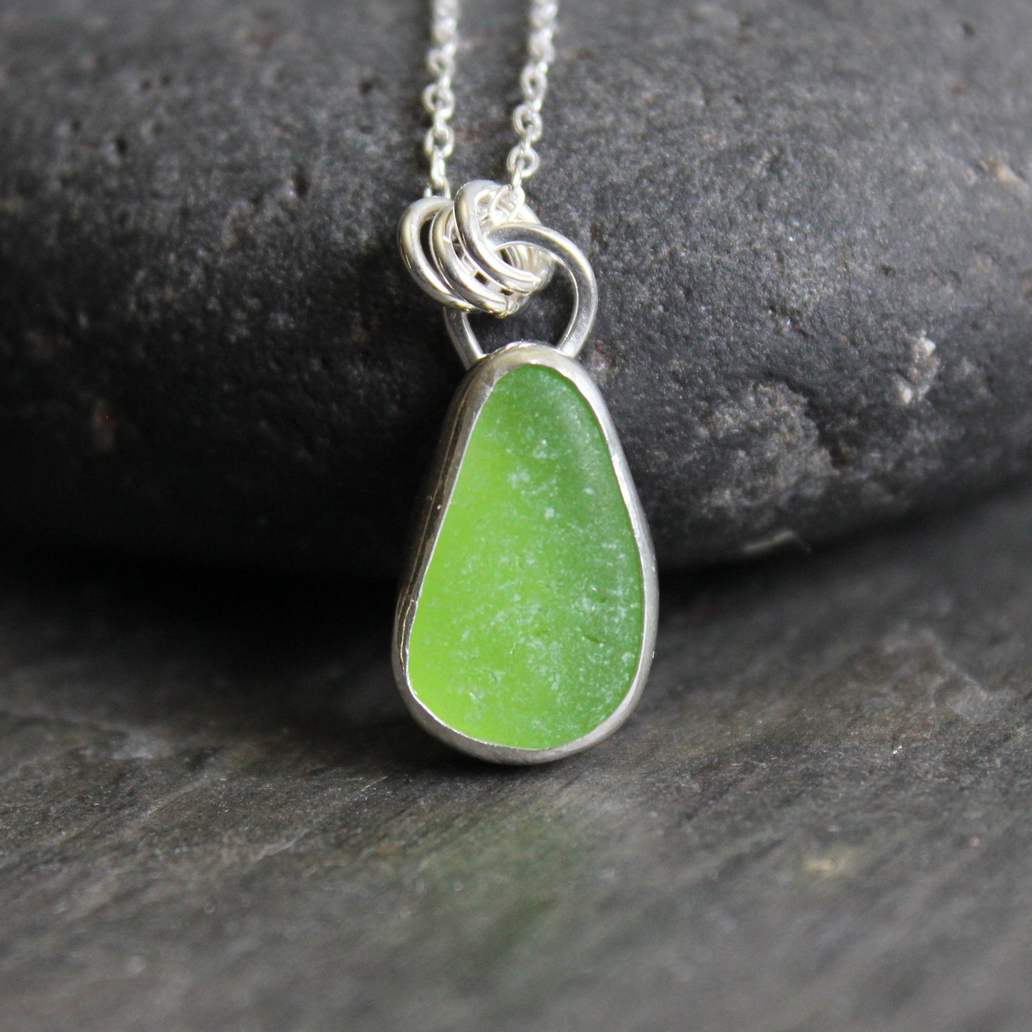 Green sea glass teardrop pendant necklace on a dark stone surface