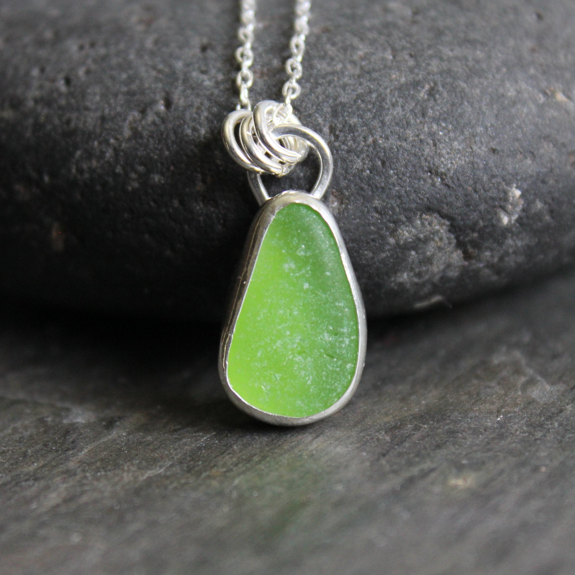 Green sea glass teardrop pendant necklace on a dark stone surface