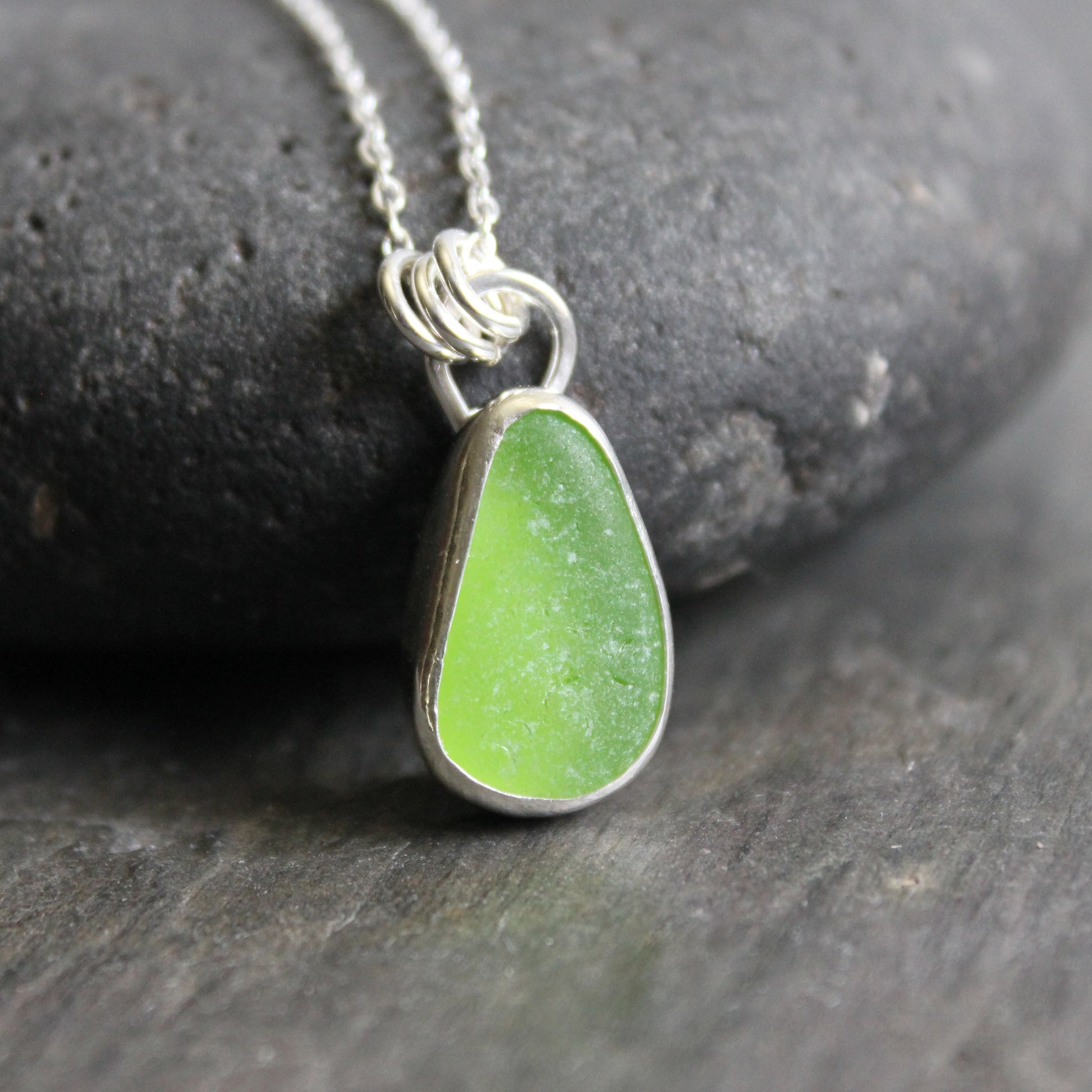 Green sea glass teardrop pendant necklace on a dark stone background