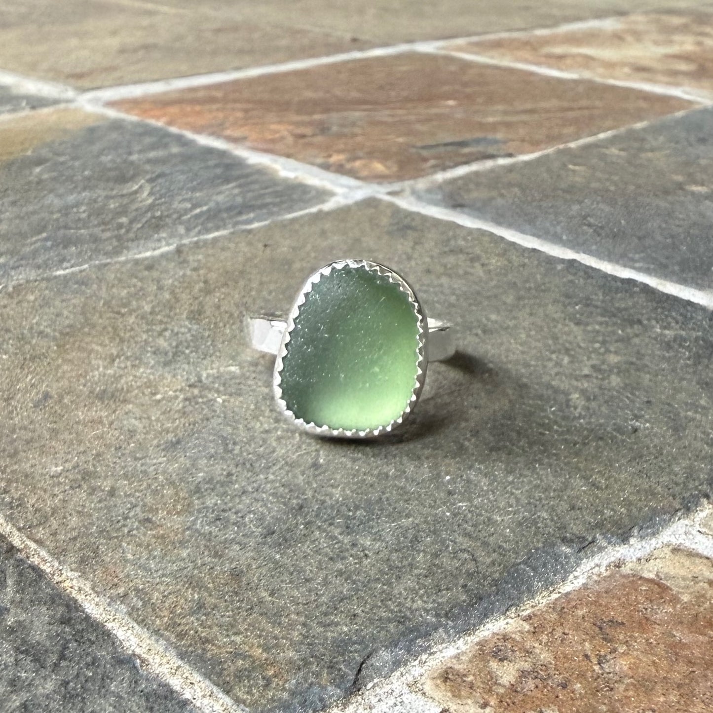 Green sea glass ring with silver band on a gray stone surface