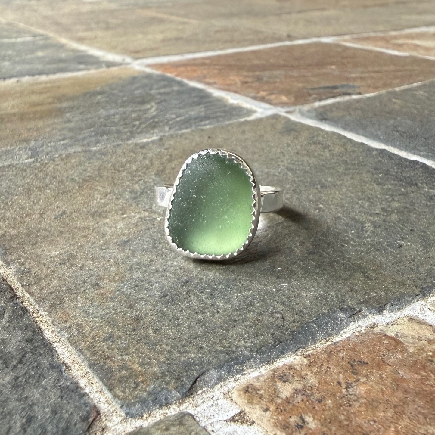 Green sea glass ring with silver band on a gray stone surface