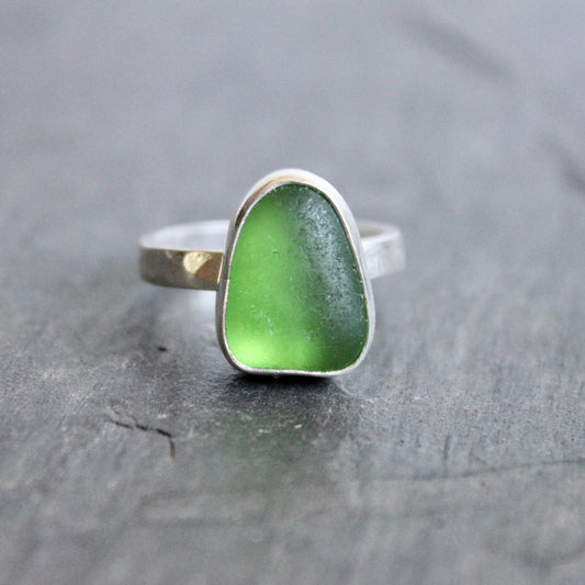 Green sea glass ring with silver setting on a dark wooden surface