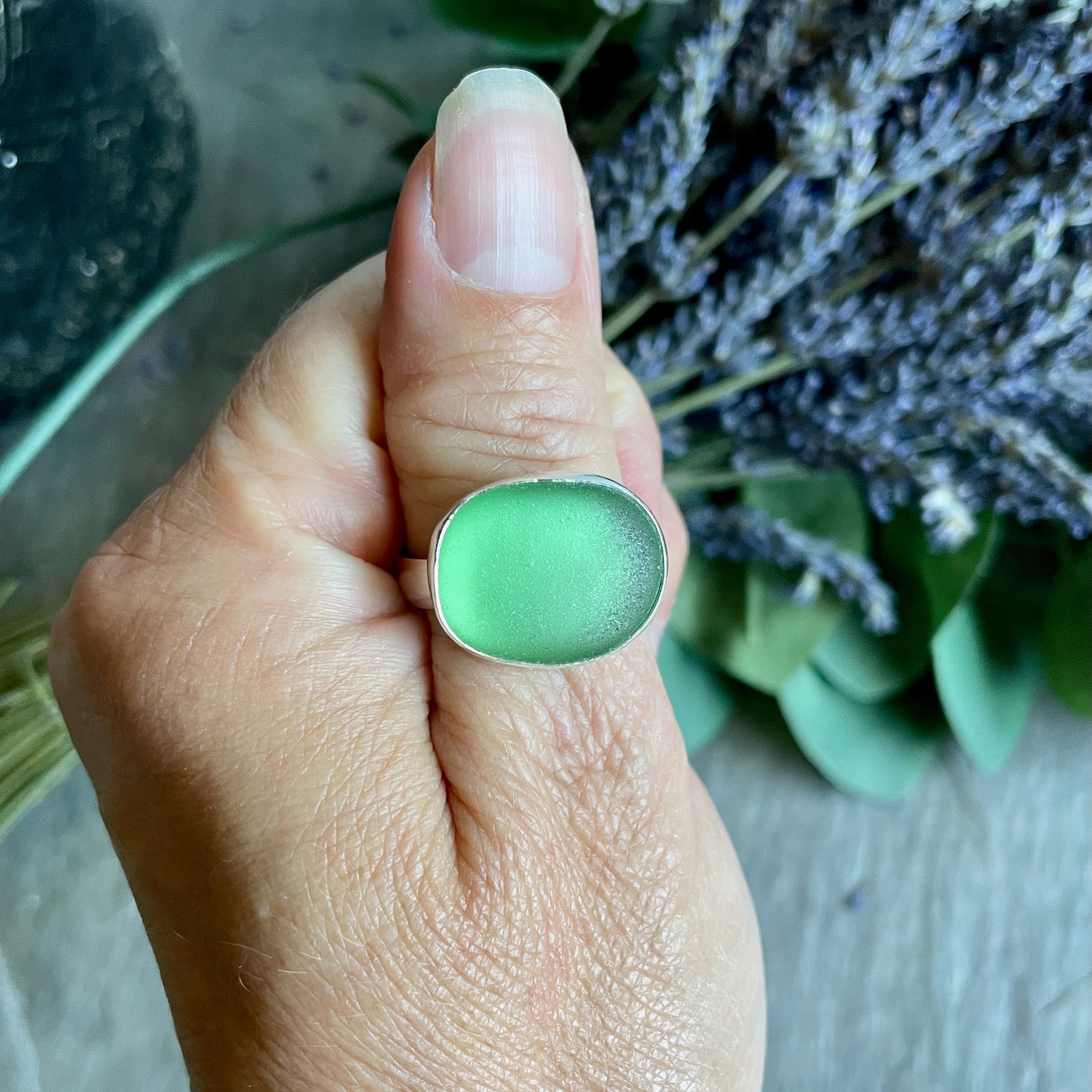 Hand wearing a green sea glass ring with lavender in the background