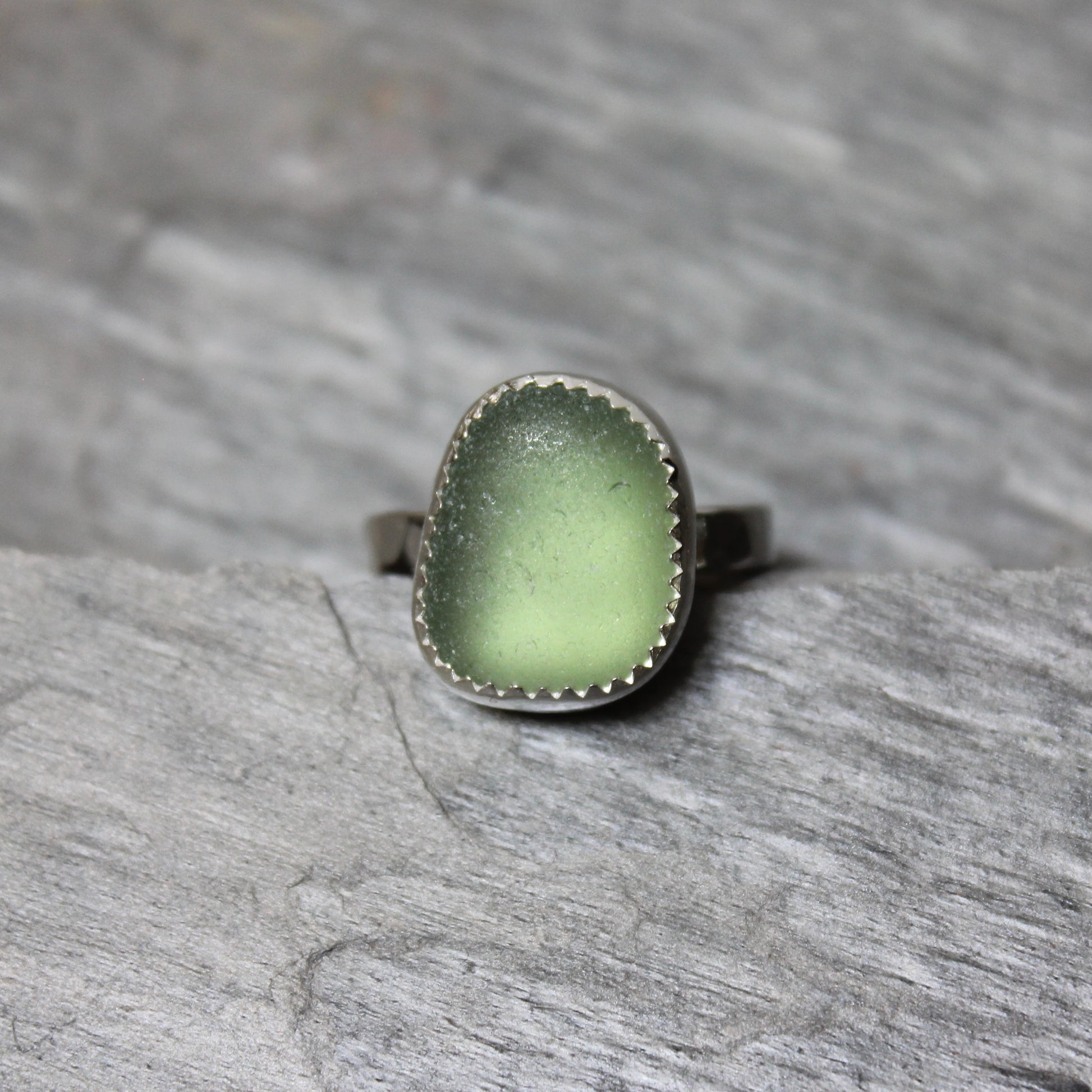 Green sea glass ring with silver band on a gray stone surface