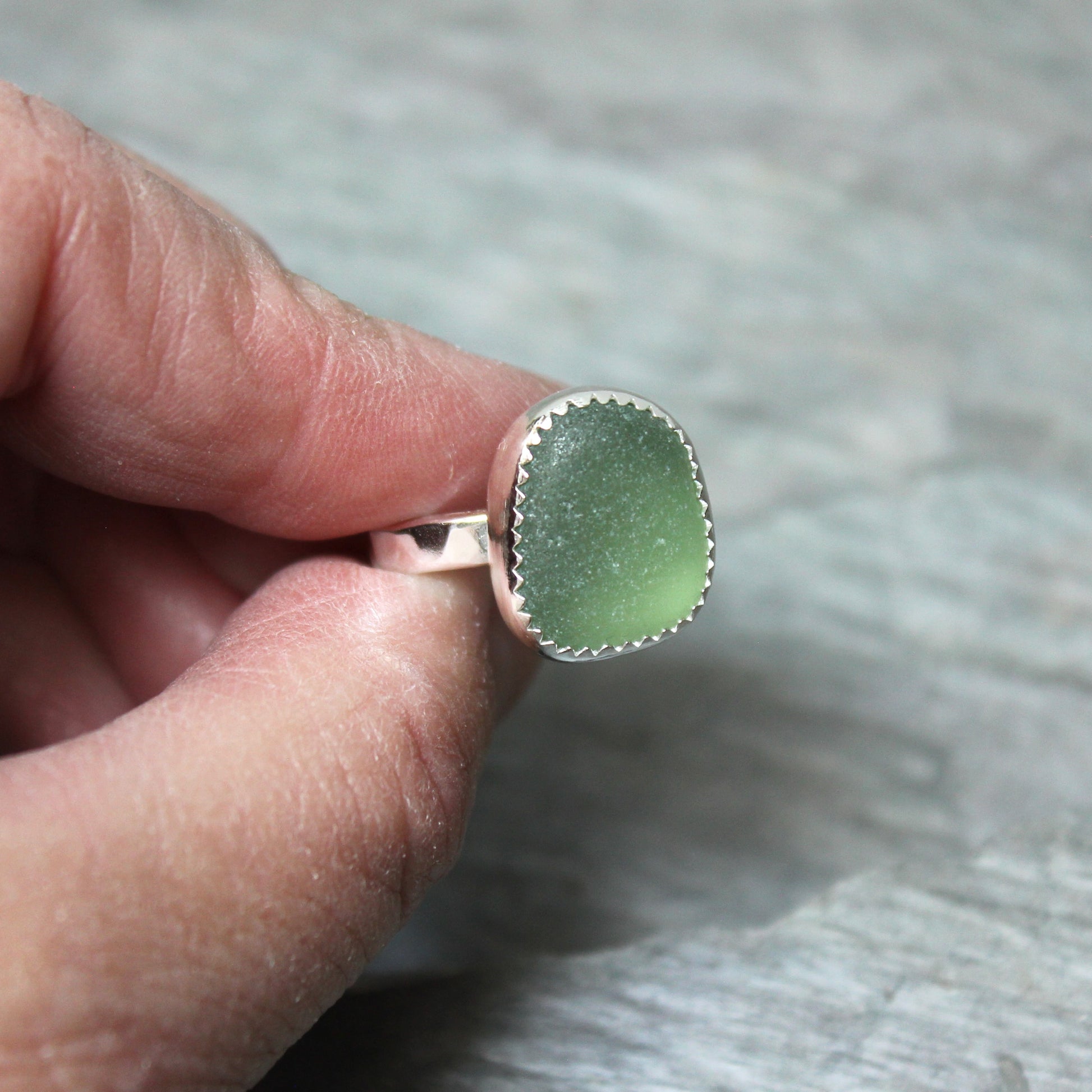 Green sea glass ring with silver setting held between fingers against a neutral background