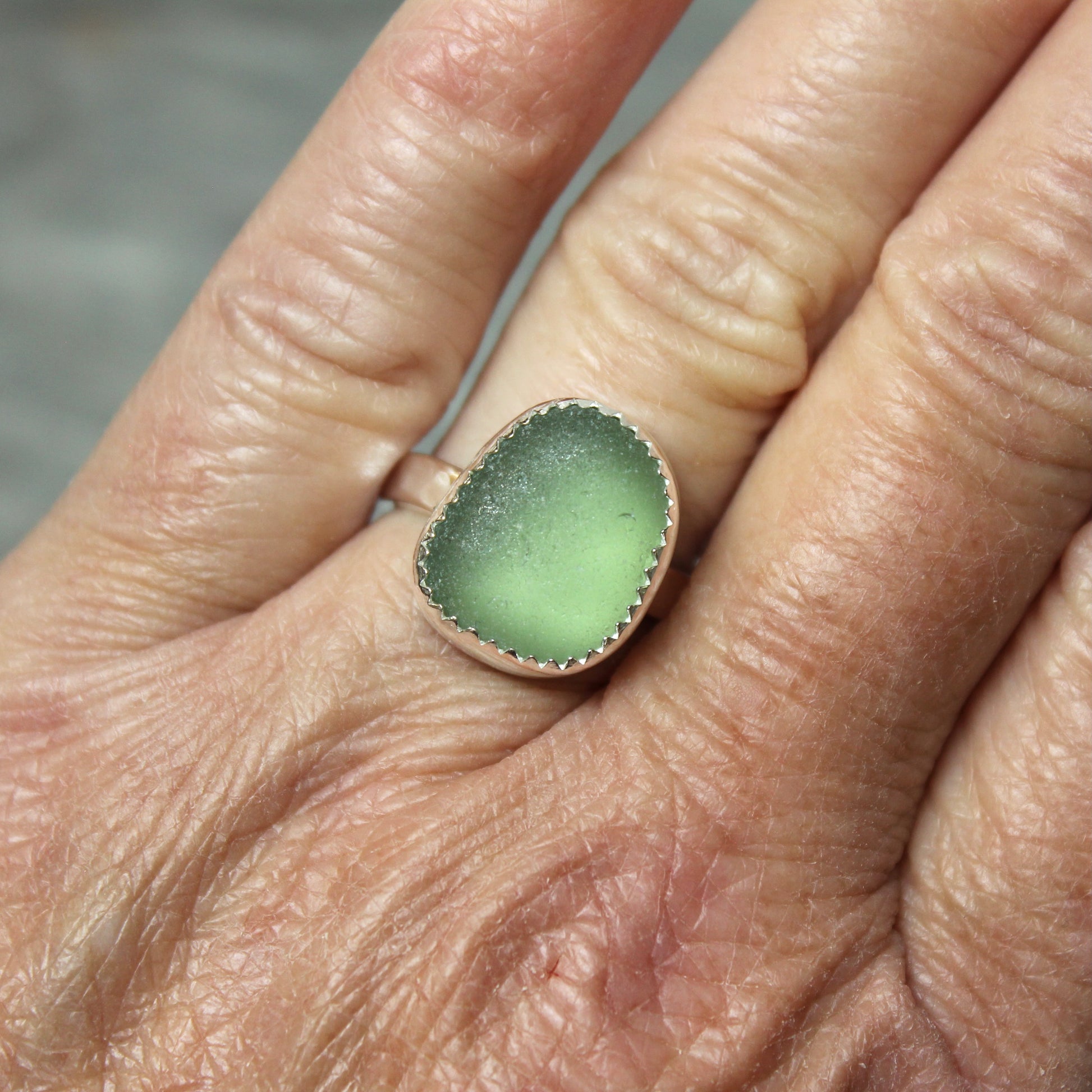 Green sea glass ring on a person's finger with a blurred background