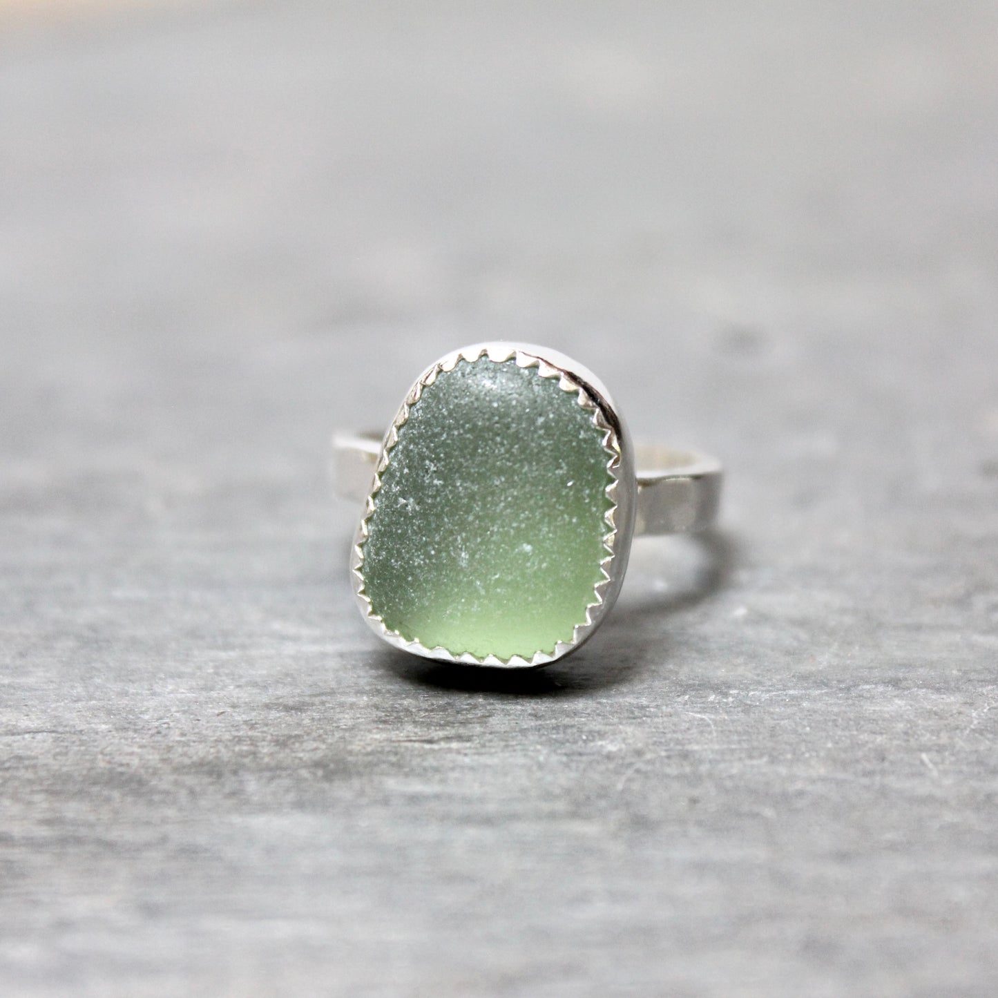 Green sea glass ring with silver band on a gray stone surface