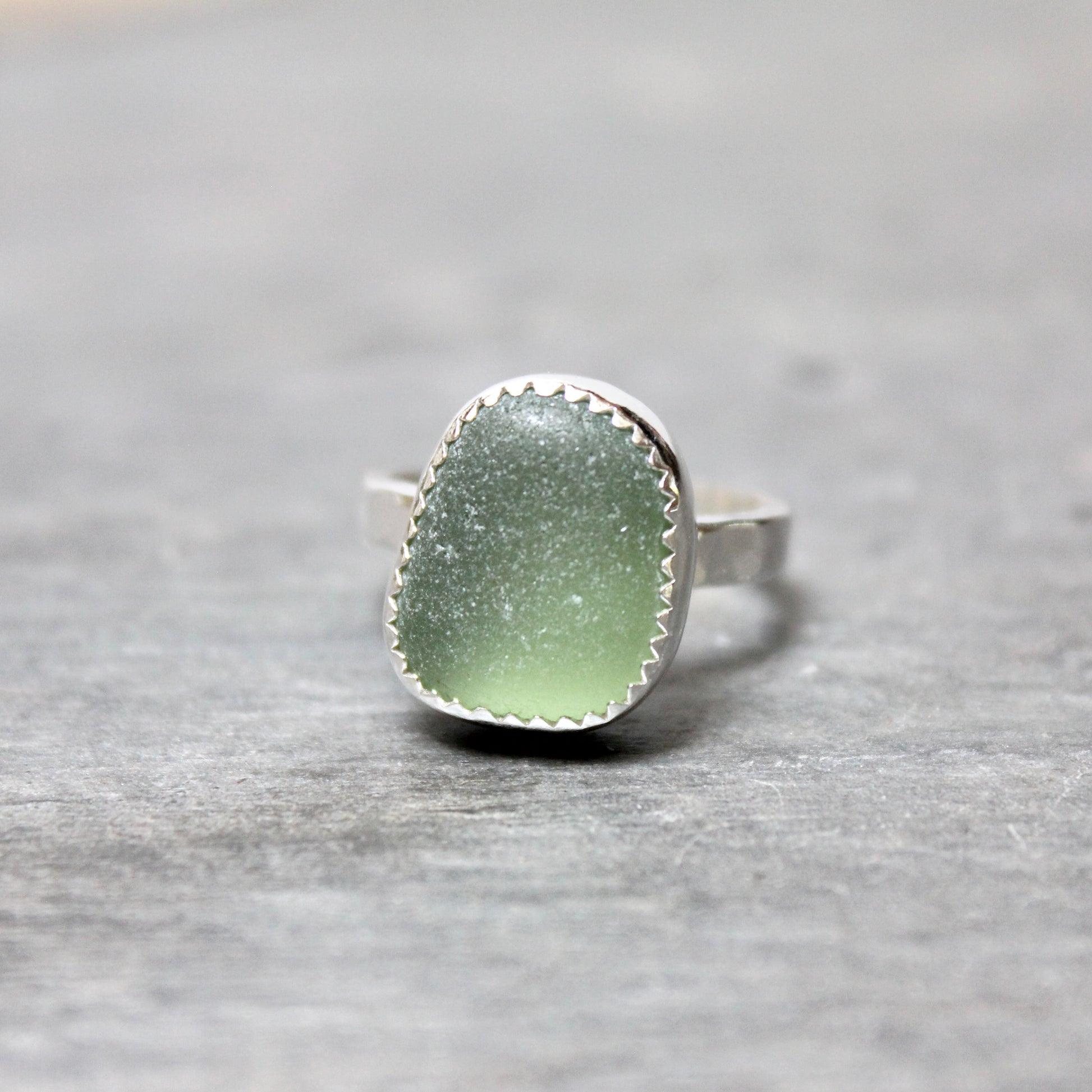 Green sea glass ring with silver band on a gray stone surface