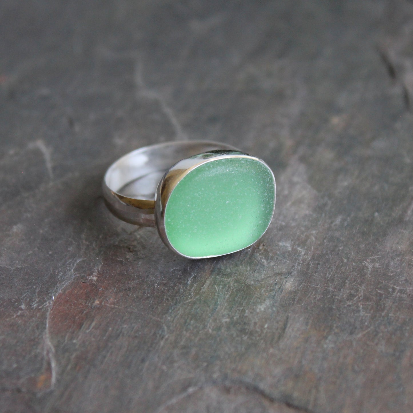 Huge green sea glass ring with silver band on a textured dark surface.