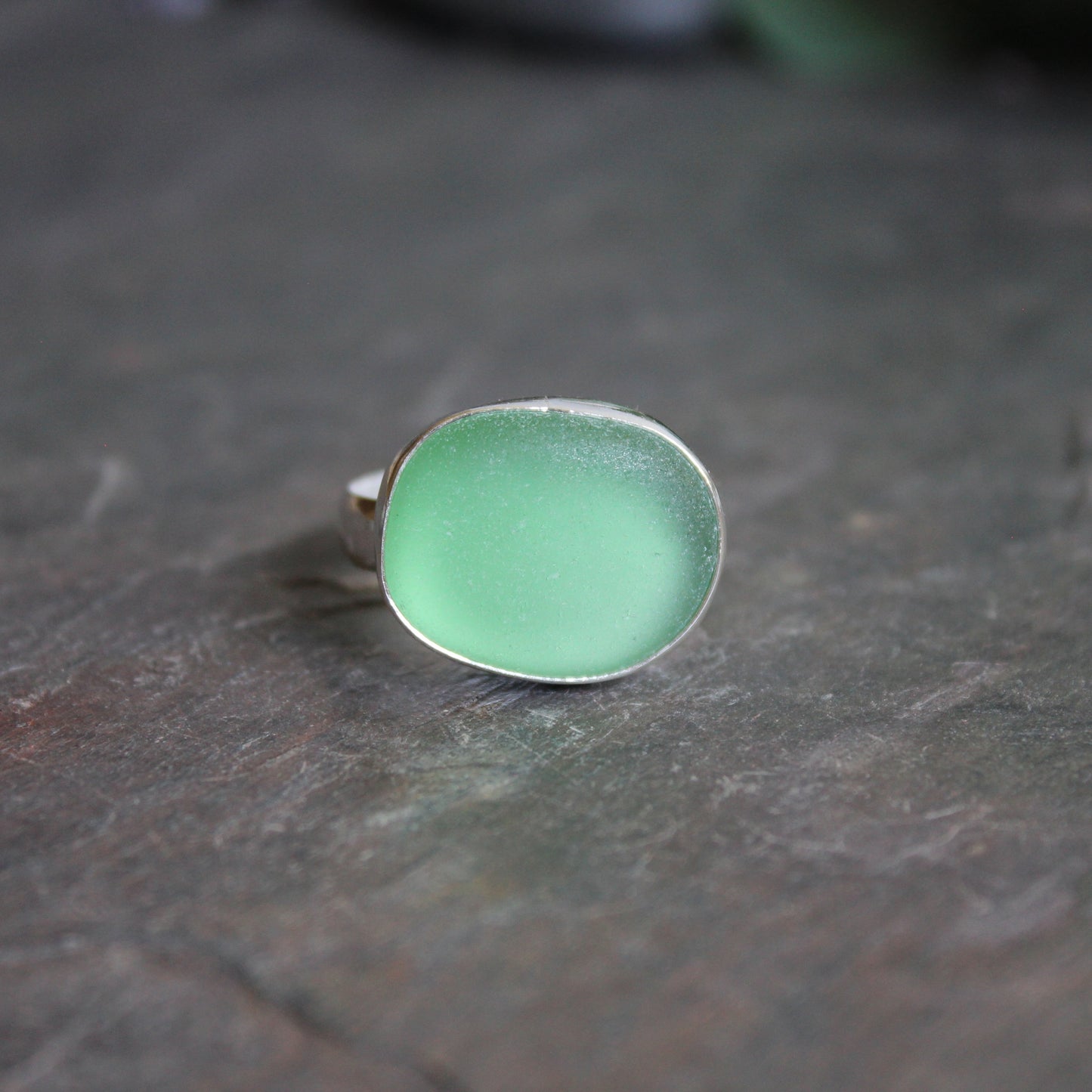 Huge green sea glass ring with silver band on a textured dark surface.