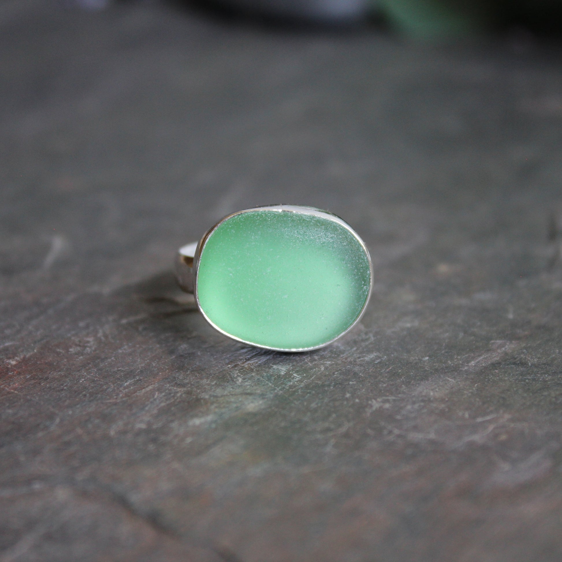 Huge green sea glass ring with silver band on a textured dark surface.