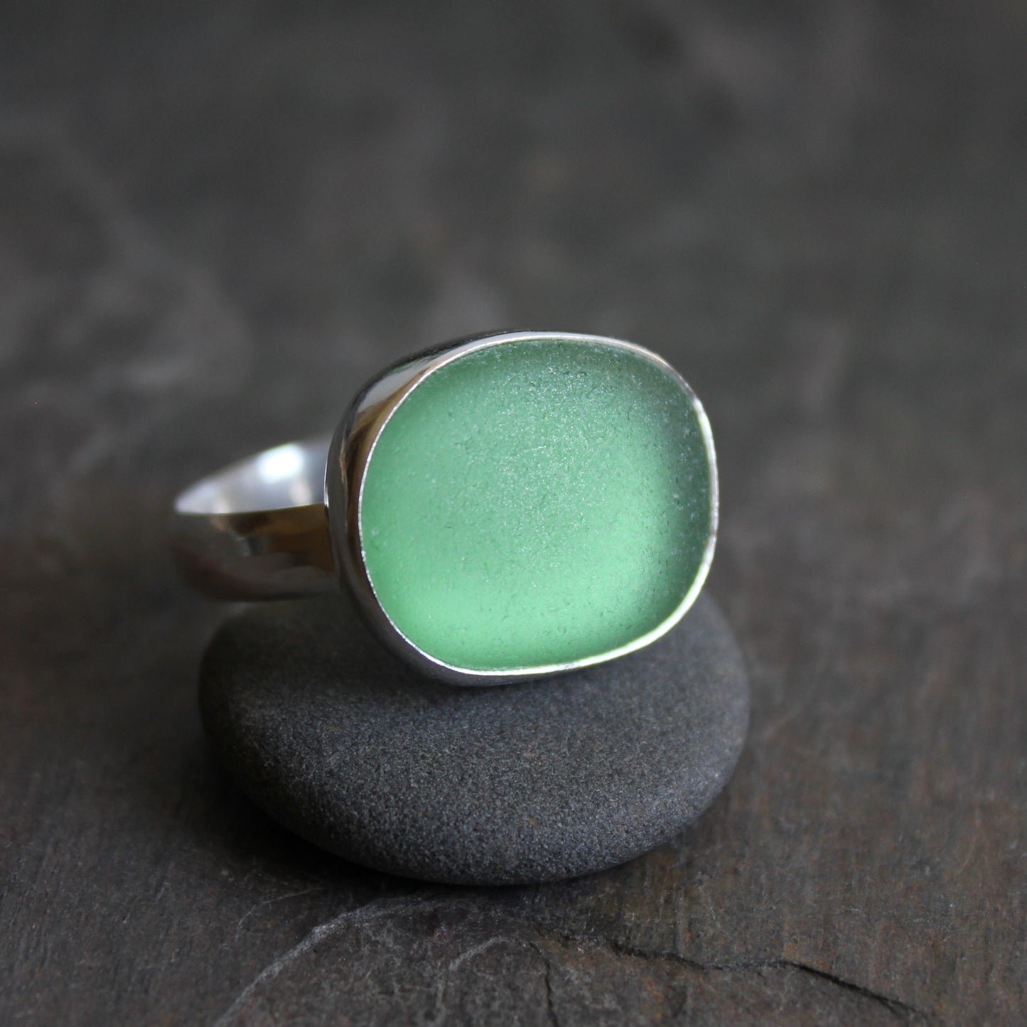  Huge green sea glass ring with silver band on a dark stone surface
