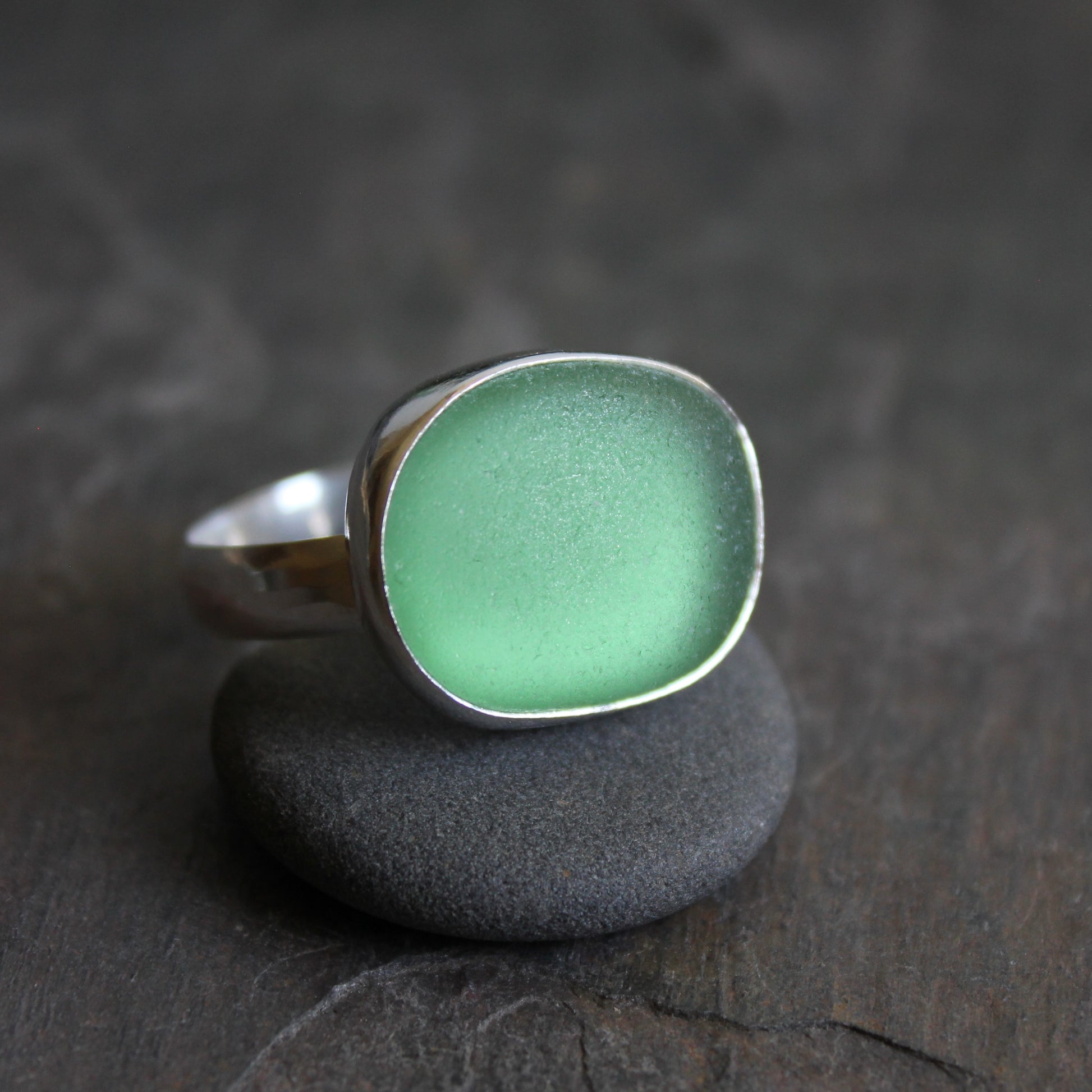  Huge green sea glass ring with silver band on a dark stone surface