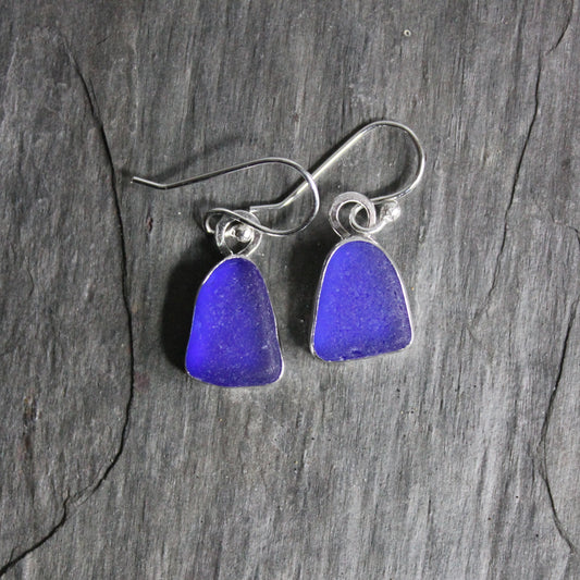 These are small dangly cobalt blue sea glass earrings that are set in a fine and sterling silver bezel setting on silver ear wires. 