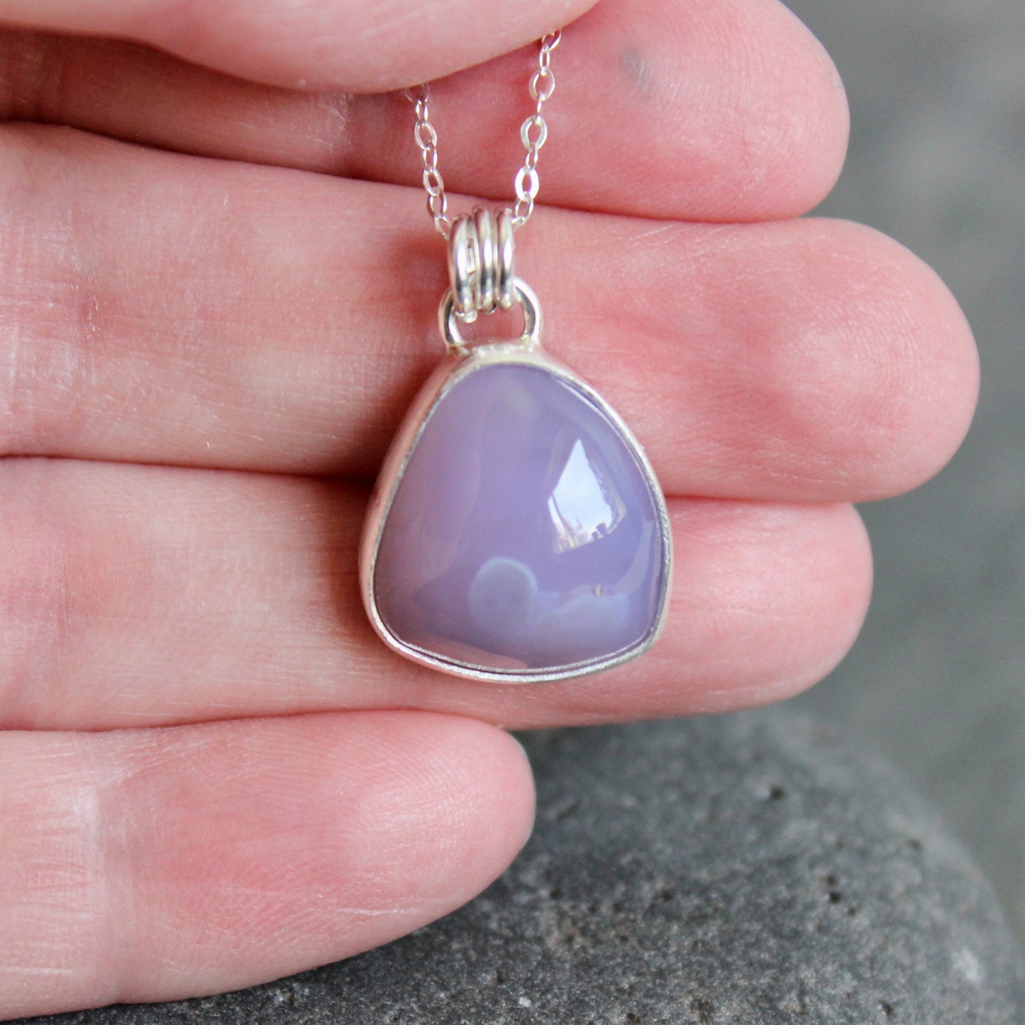 Purple teardrop pendant on a silver chain held between fingers