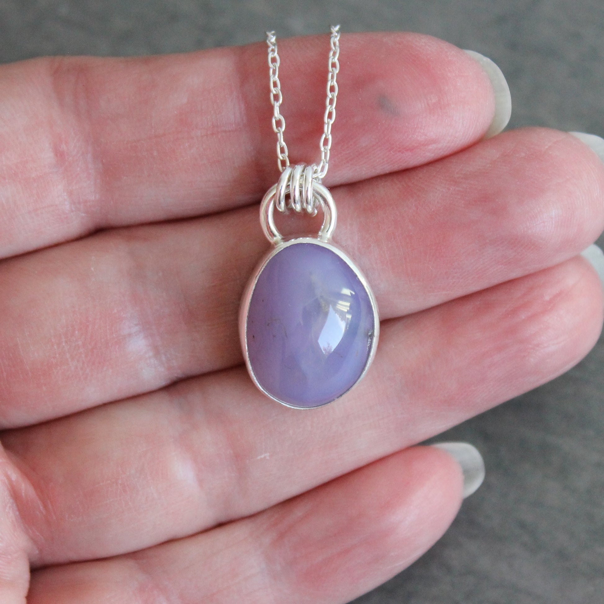 Purple holley blue agate pendant necklace on a hand against a neutral background