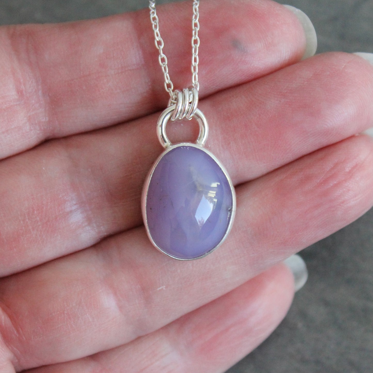 Purple holley blue agate pendant on a silver chain held in a hand.