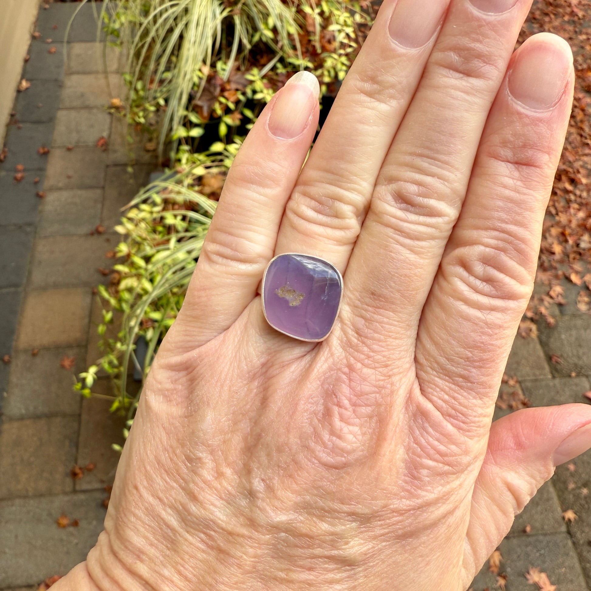 Hand wearing a purple holley blue agate ring with a garden in the background