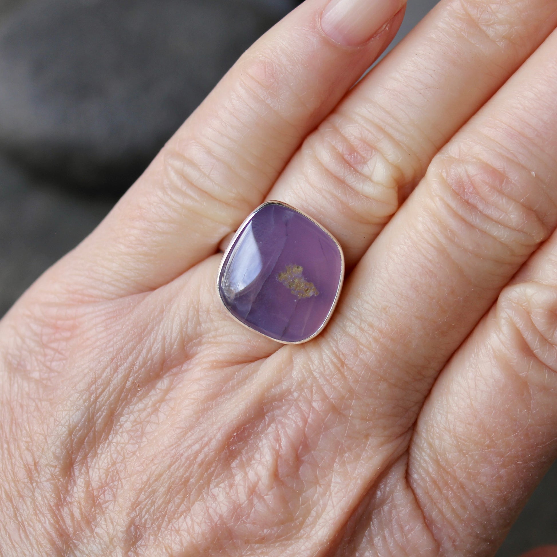 Hand wearing a ring with a holley blue agate on a neutral background
