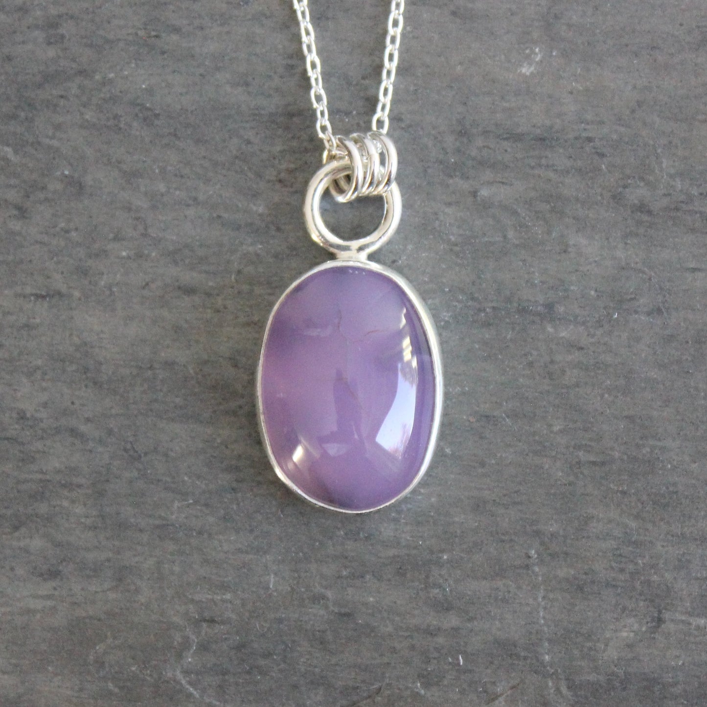 Necklace with a purple holley blue agate pendant on a gray stone surface
