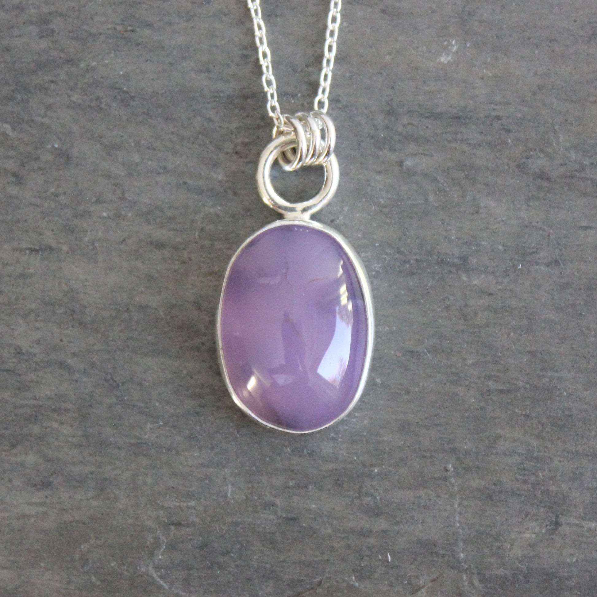 Necklace with a purple holley blue agate pendant on a gray stone surface