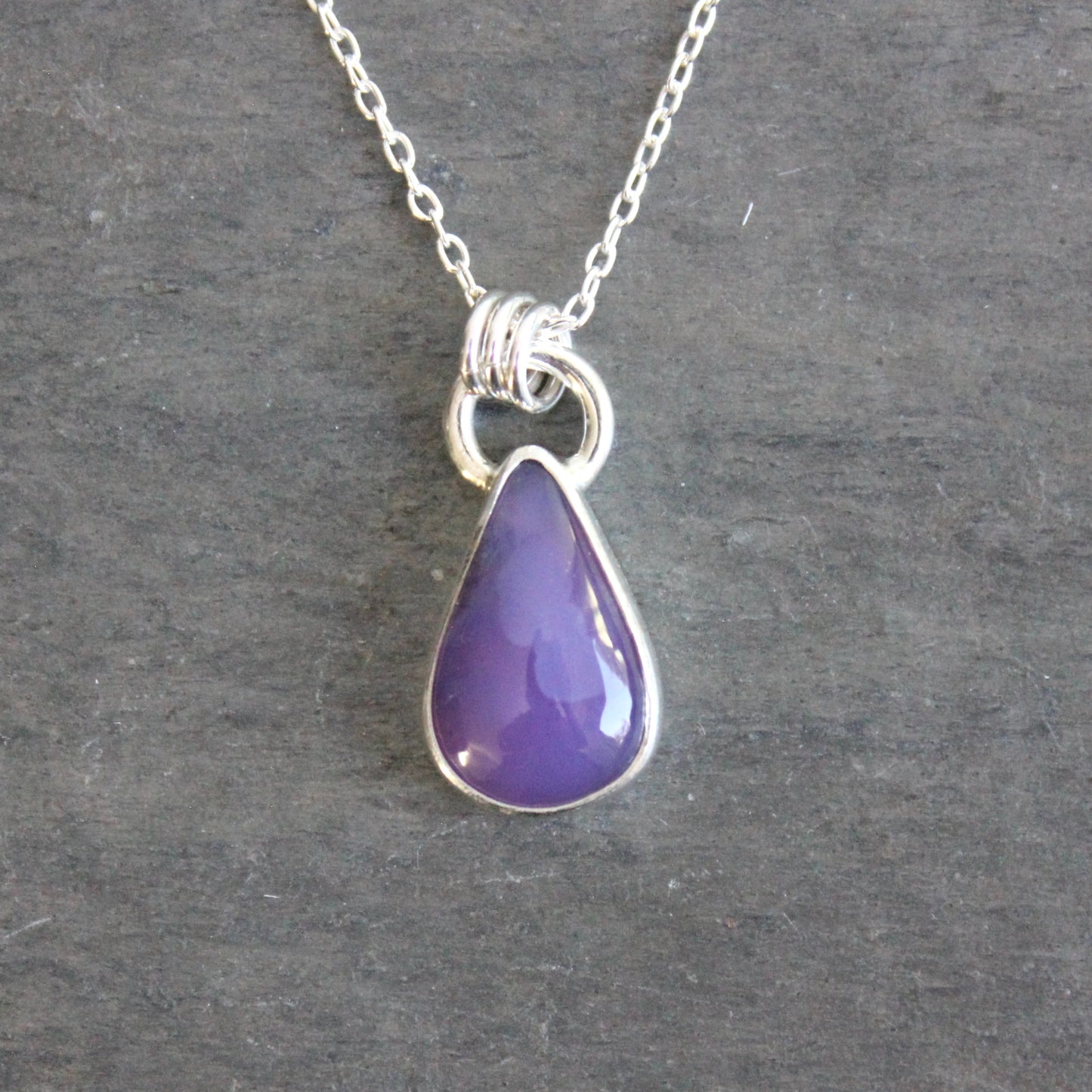 Purple teardrop pendant on a silver chain against a gray background