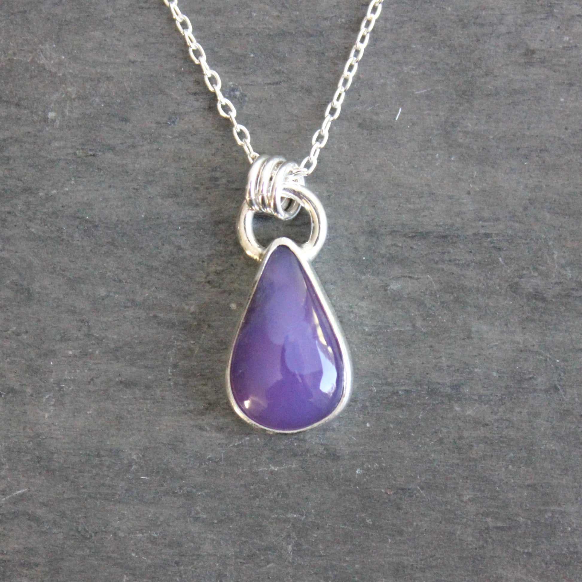 Purple teardrop pendant on a silver chain against a gray background