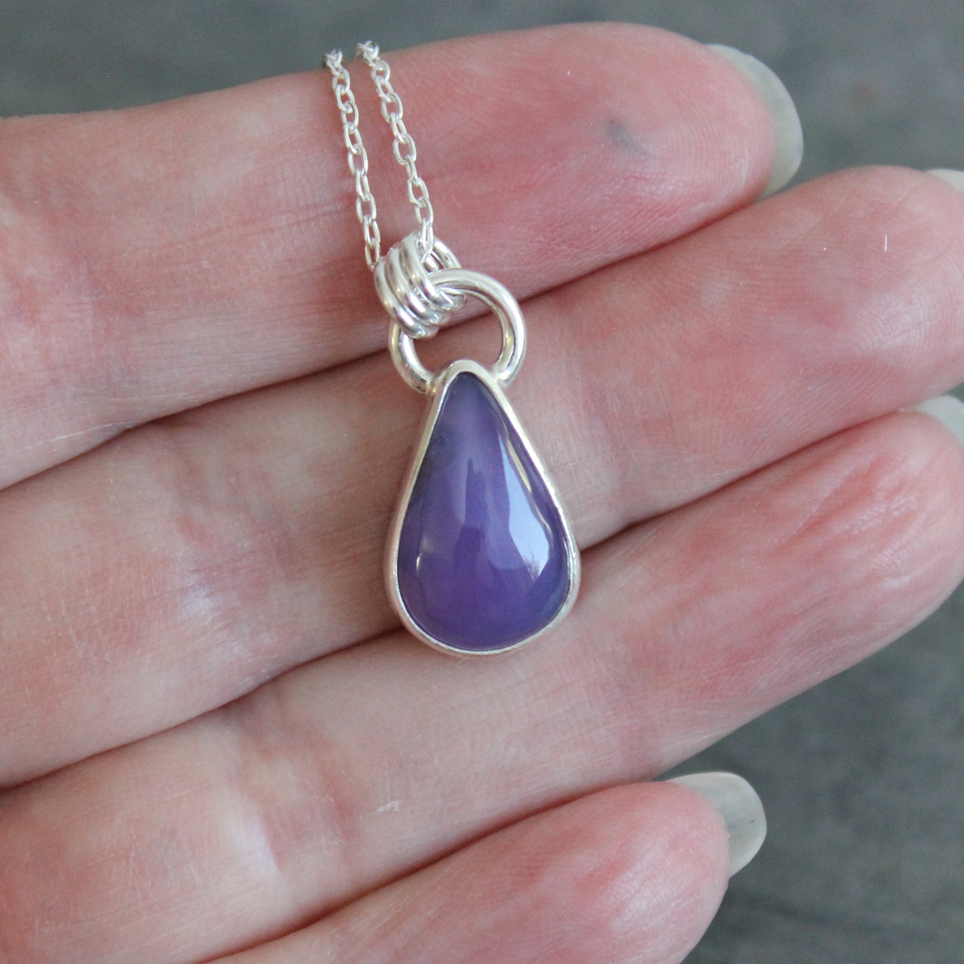 Purple teardrop pendant on a silver chain held in a hand.