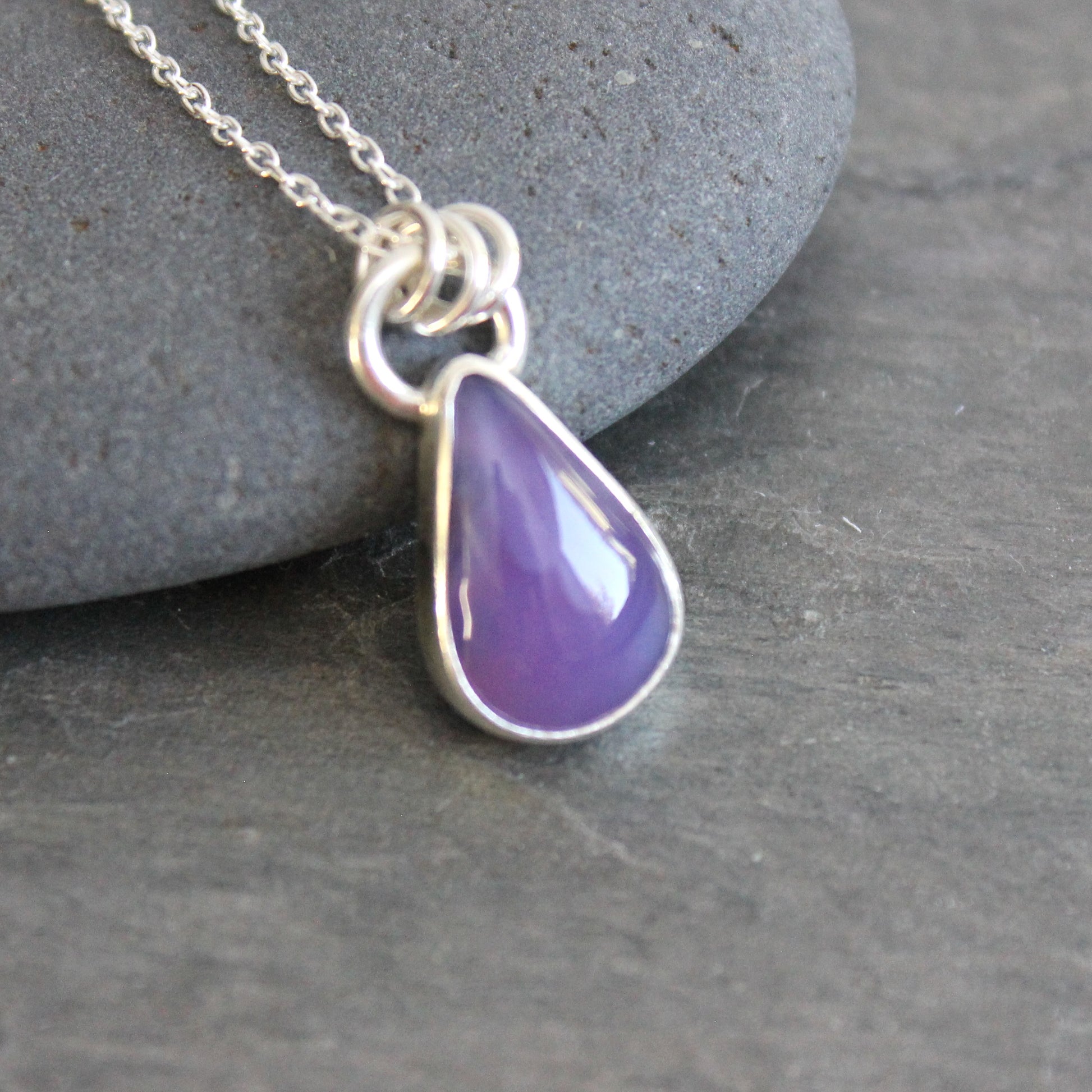 Purple teardrop holley blue agate pendant on a silver chain against a gray stone background