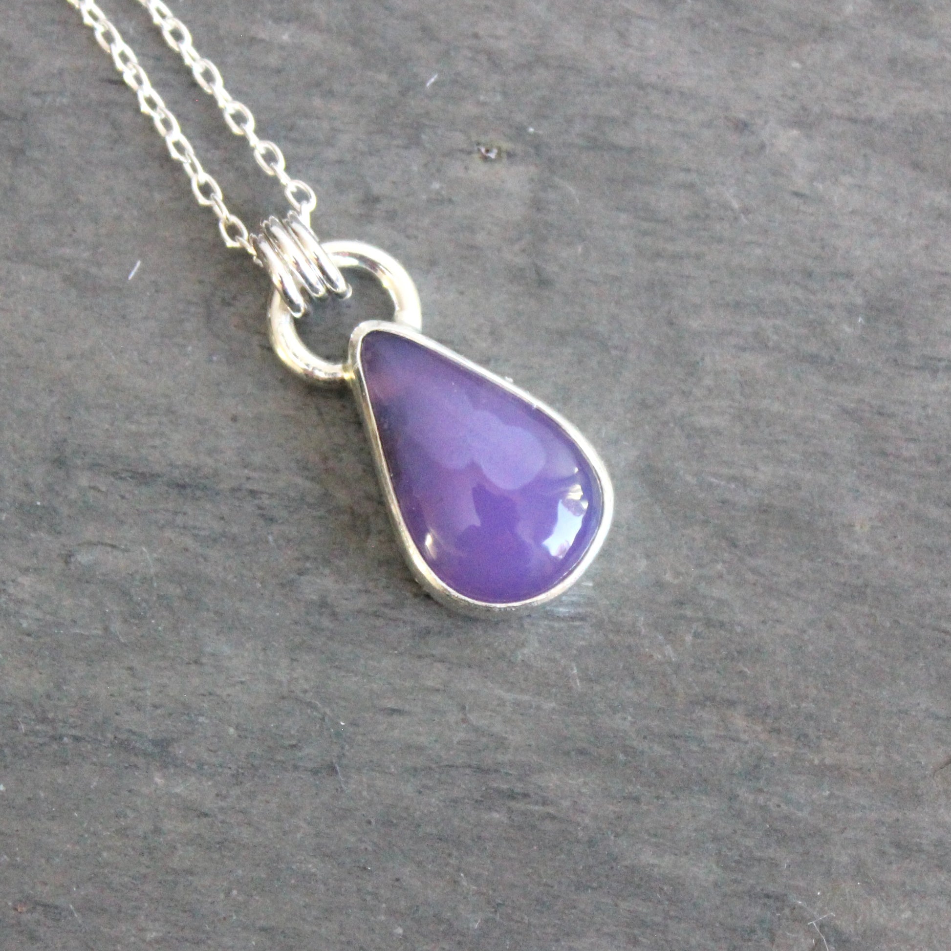 Purple teardrop pendant on a silver chain against a gray background
