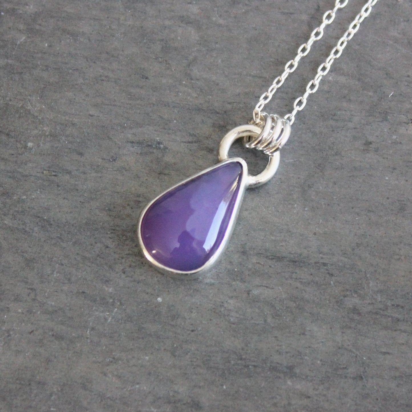 Purple teardrop pendant on a silver chain against a gray background