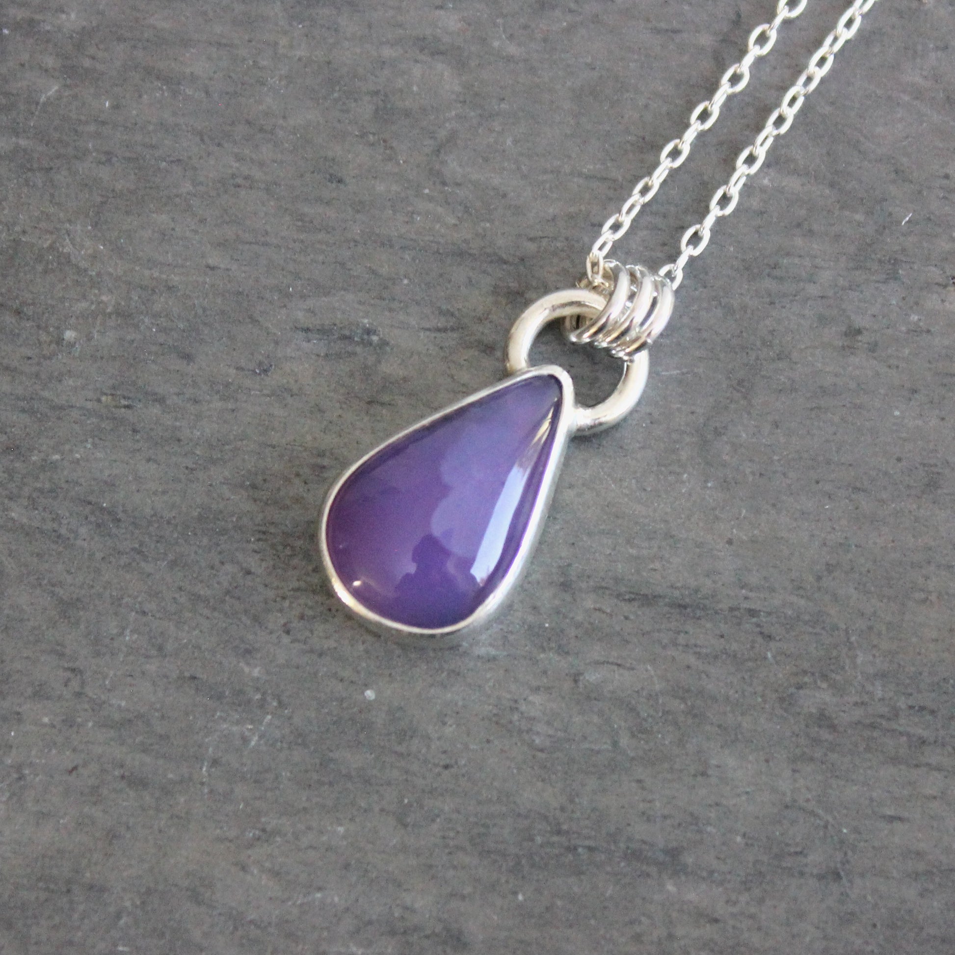 Purple teardrop pendant on a silver chain against a gray background