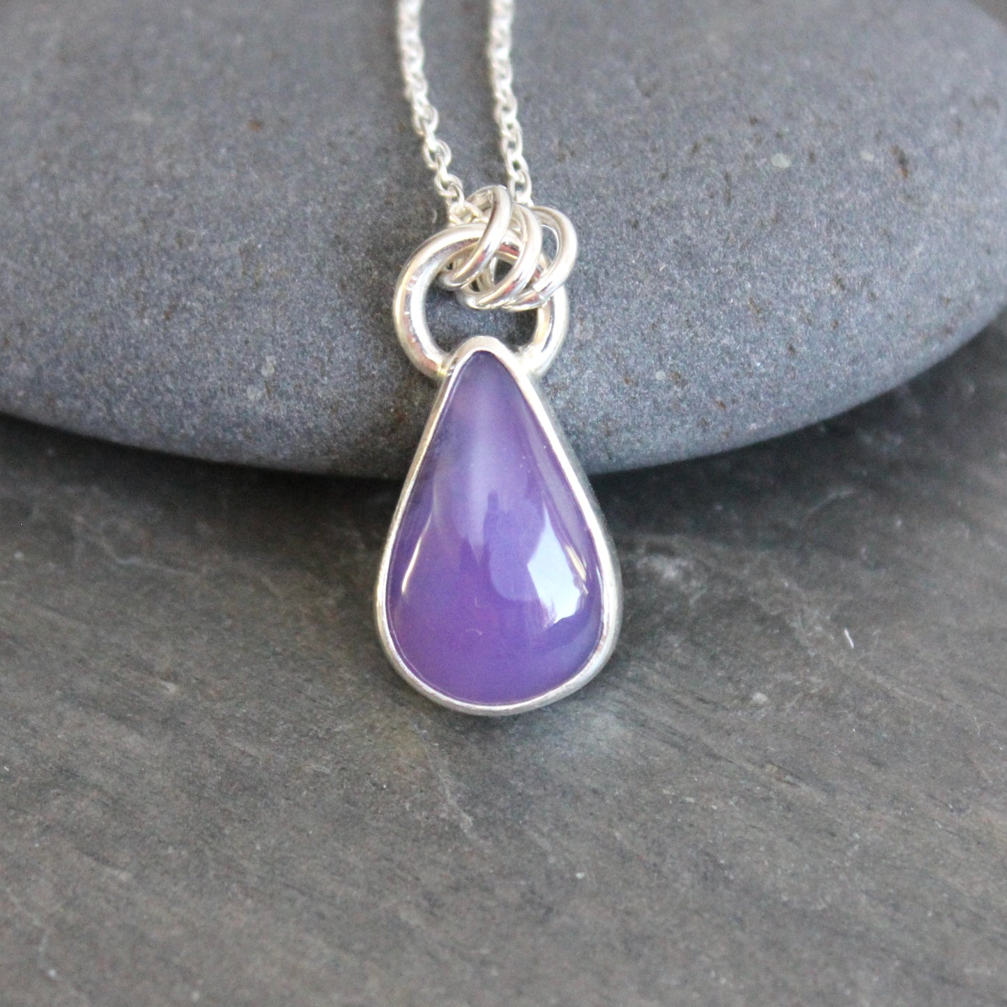 Purple holley blue agate teardrop pendant on a silver chain against a gray stone background