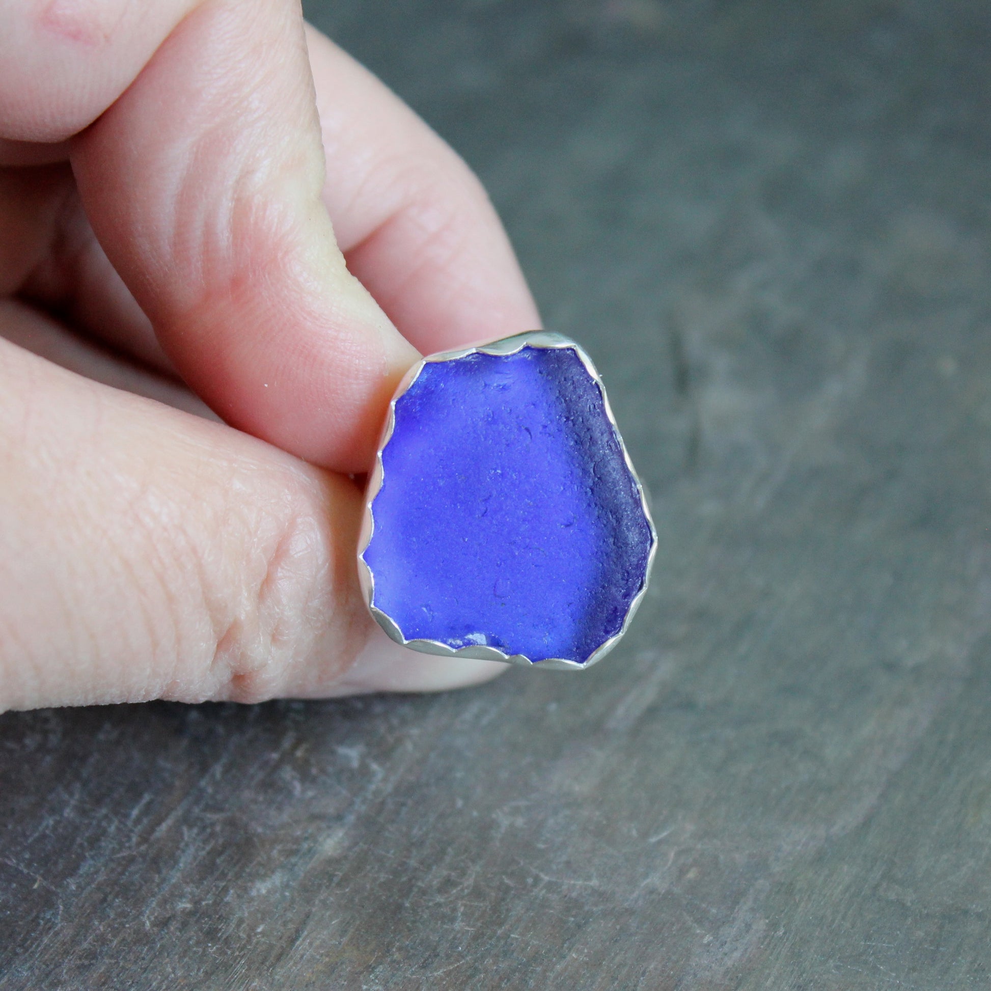 Hand holding a piece of blue sea glass ring against a dark background