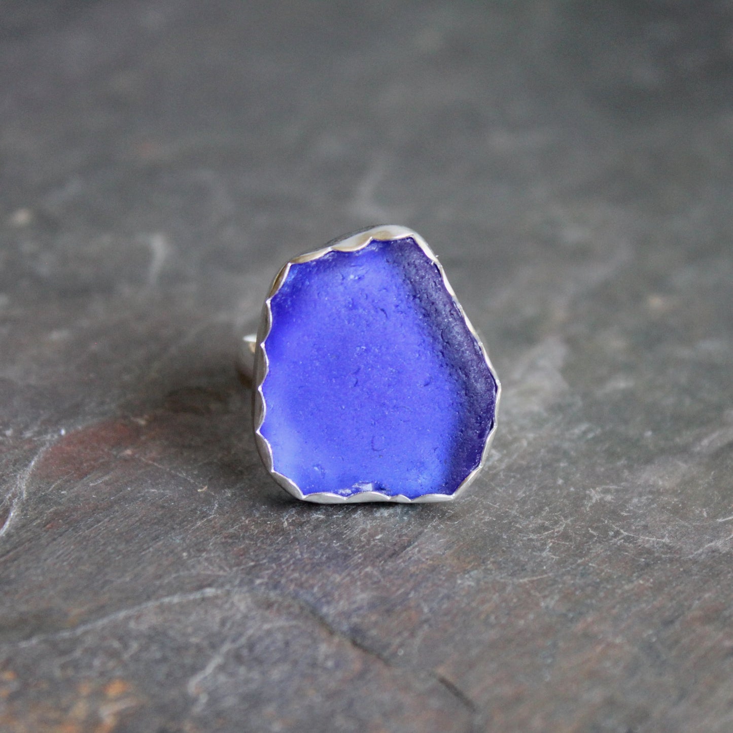 Blue sea glass ring with silver setting on a dark stone surface